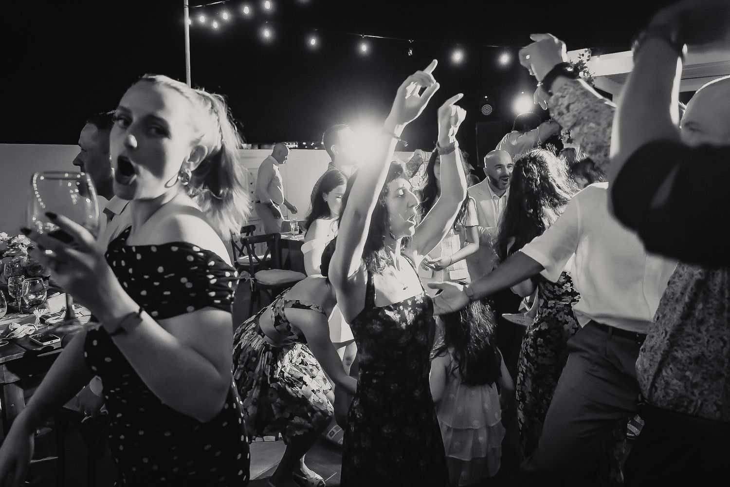Black and white photo of guests dancing joyfully at an outdoor evening wedding reception party.