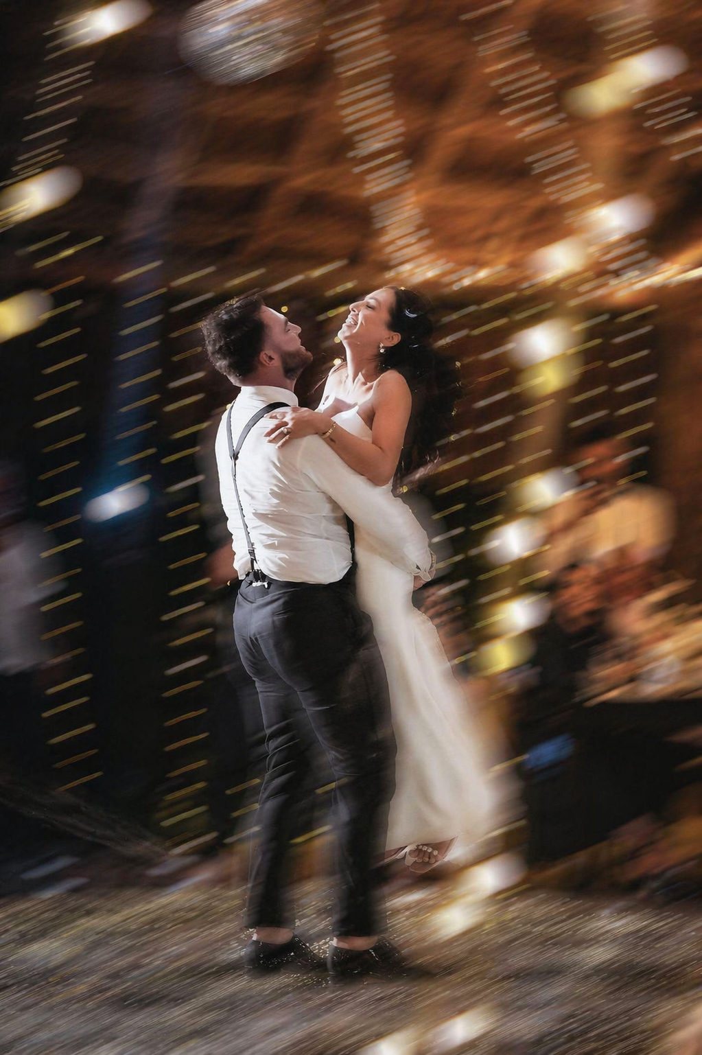 A couple shares a joyful first dance at their wedding reception, surrounded by warm bokeh lights.