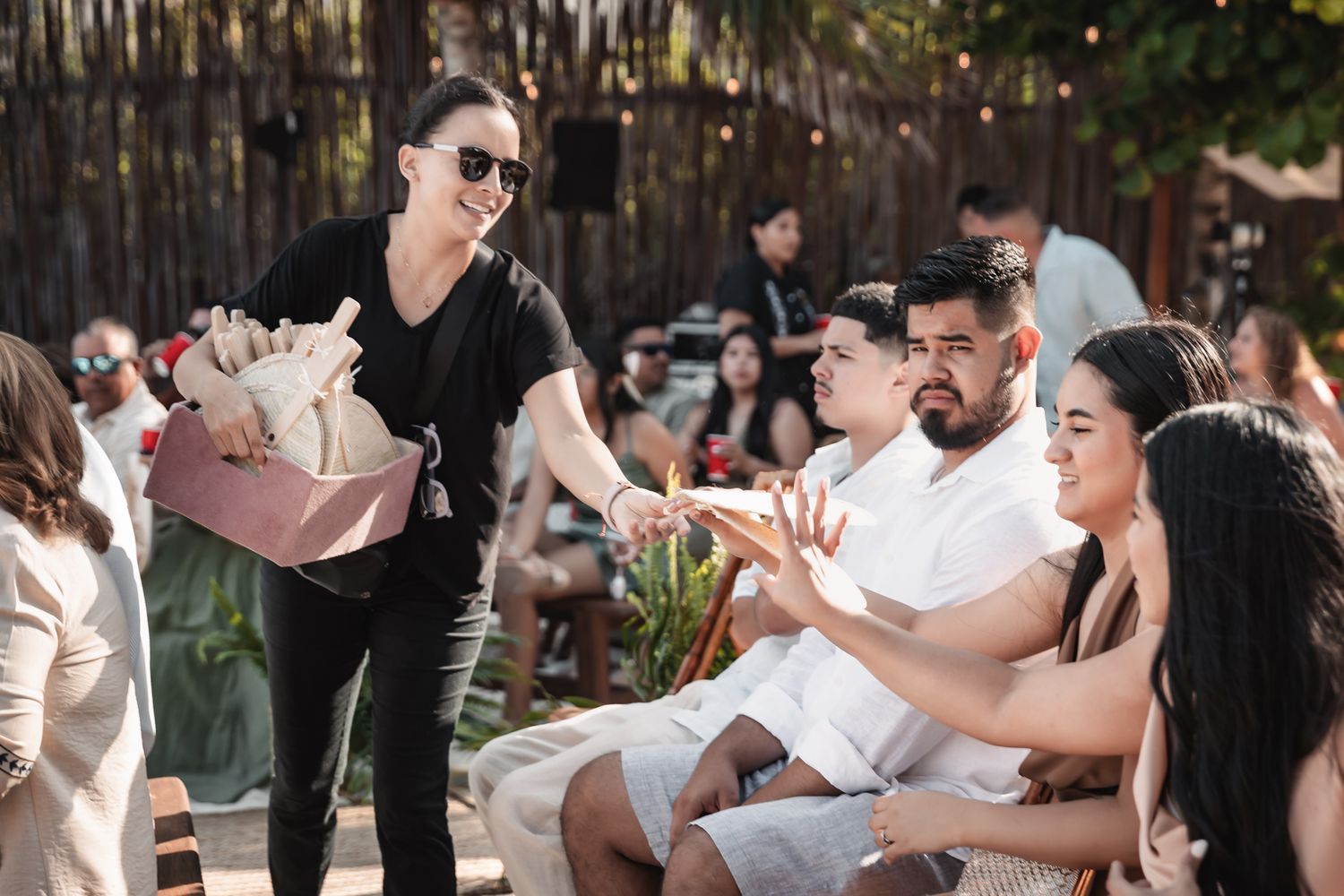 Woman in black outfit handing flowers to seated guests at an outdoor social gathering event.