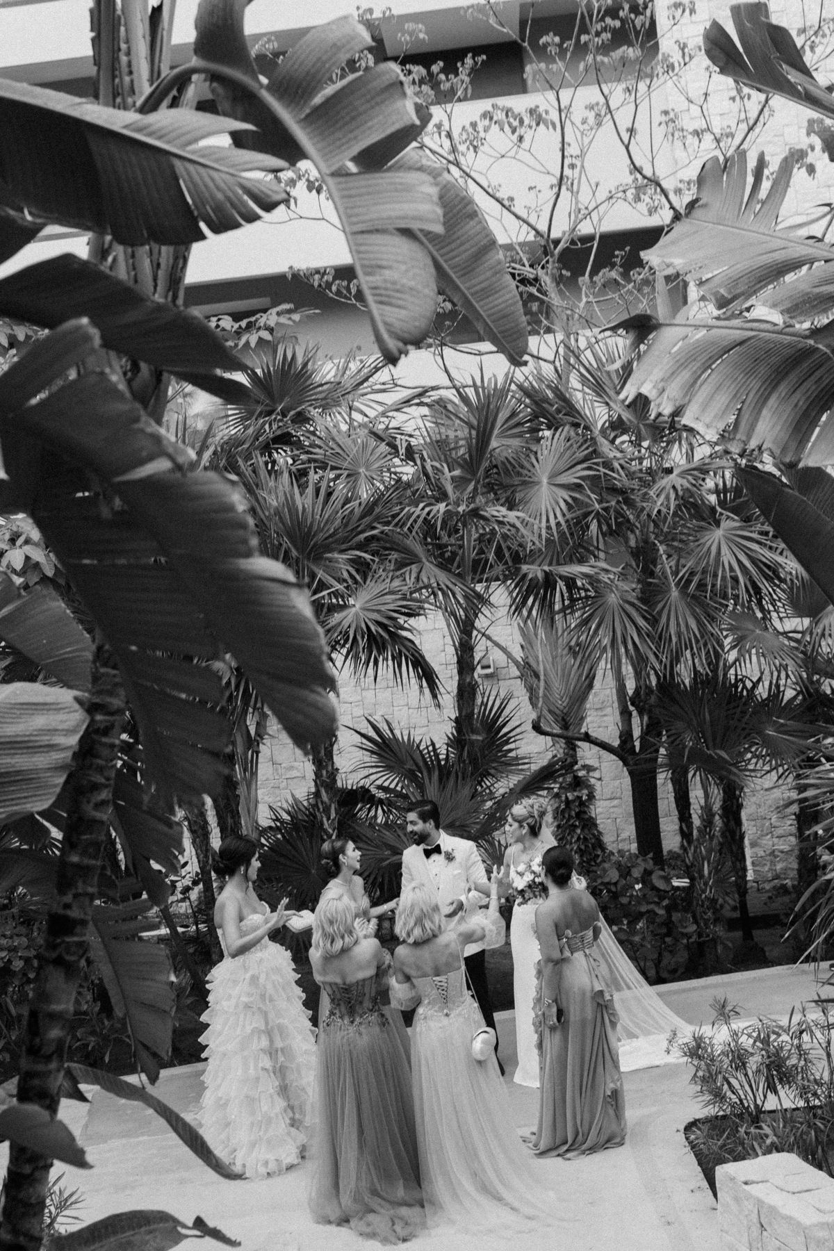 Black and white photo of a wedding ceremony outdoors surrounded by lush tropical palm trees and banana leaves.