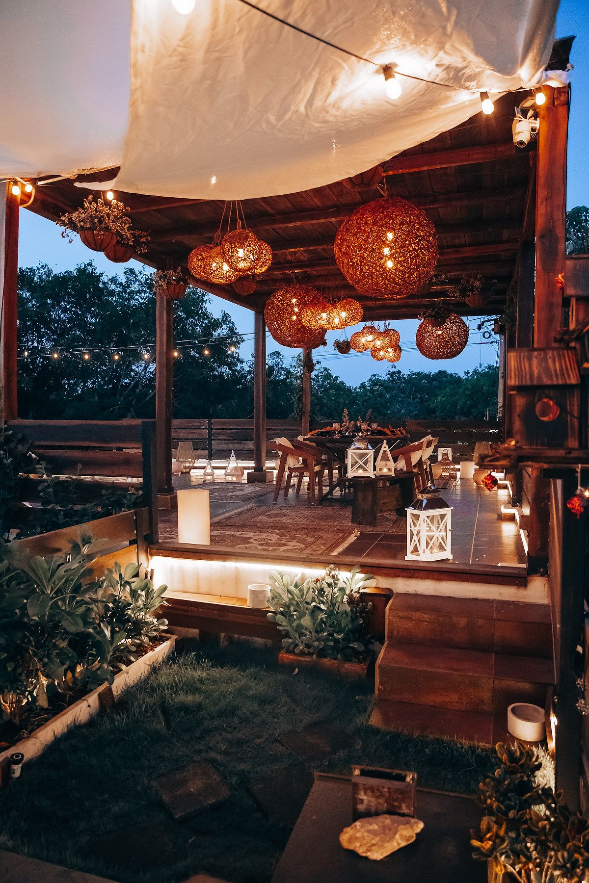 Enchanting twilight terrace with glowing wicker lanterns, string lights, and lush garden surroundings.