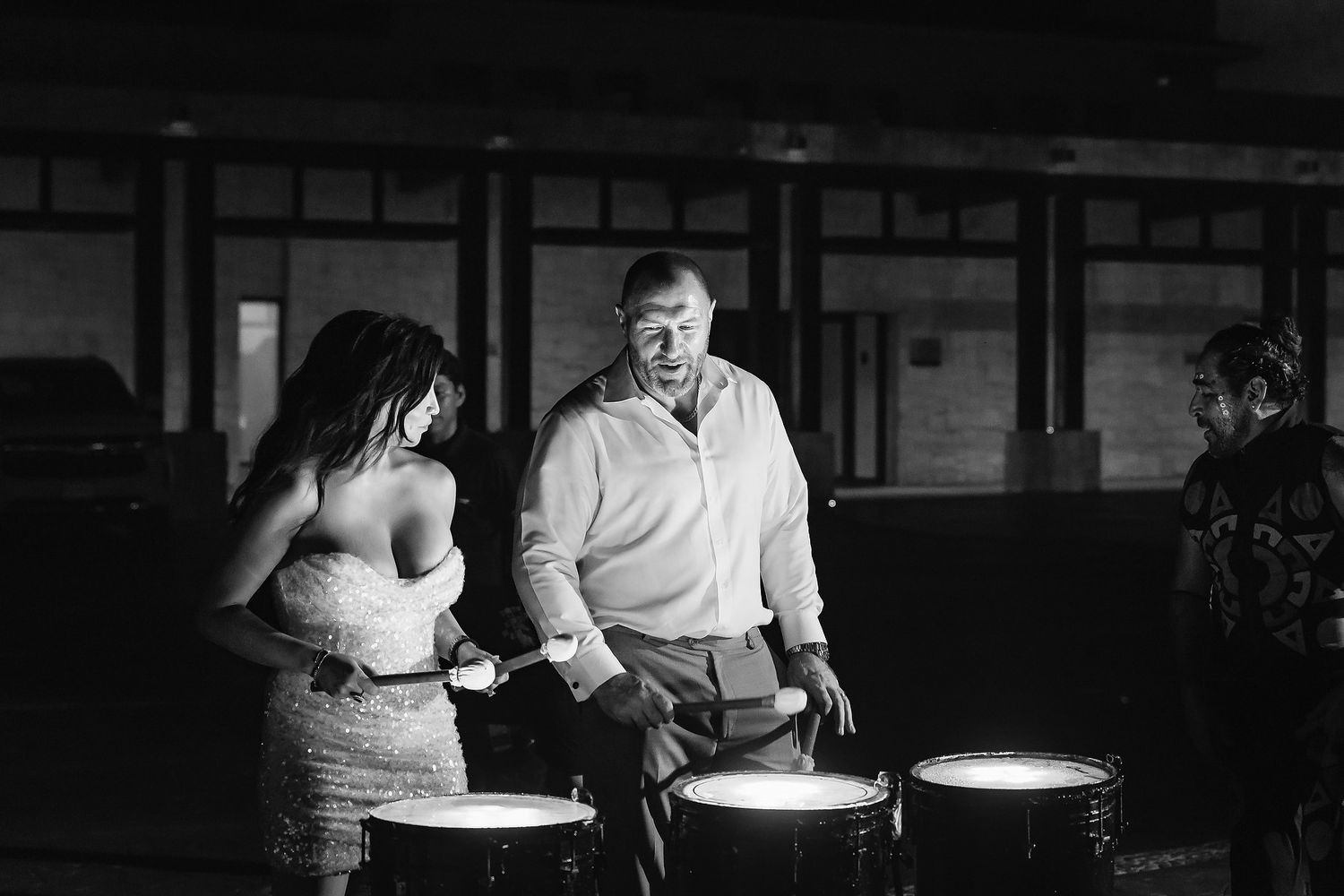 Black and white photo of a bride and groom laughing together beside illuminated drums at a wedding reception.