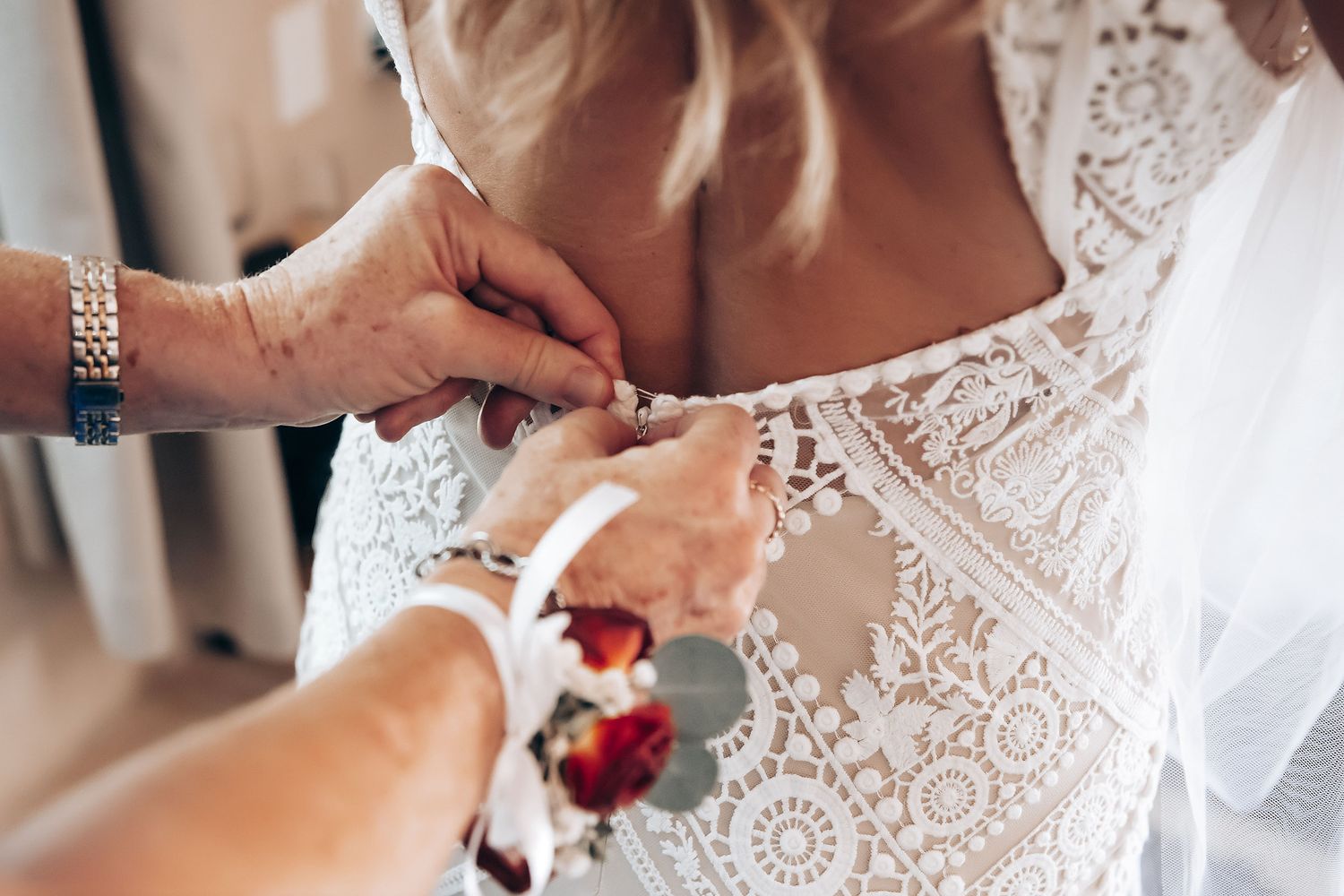 Close-up detail of delicate lace wedding dress being fastened with buttons and pearls.