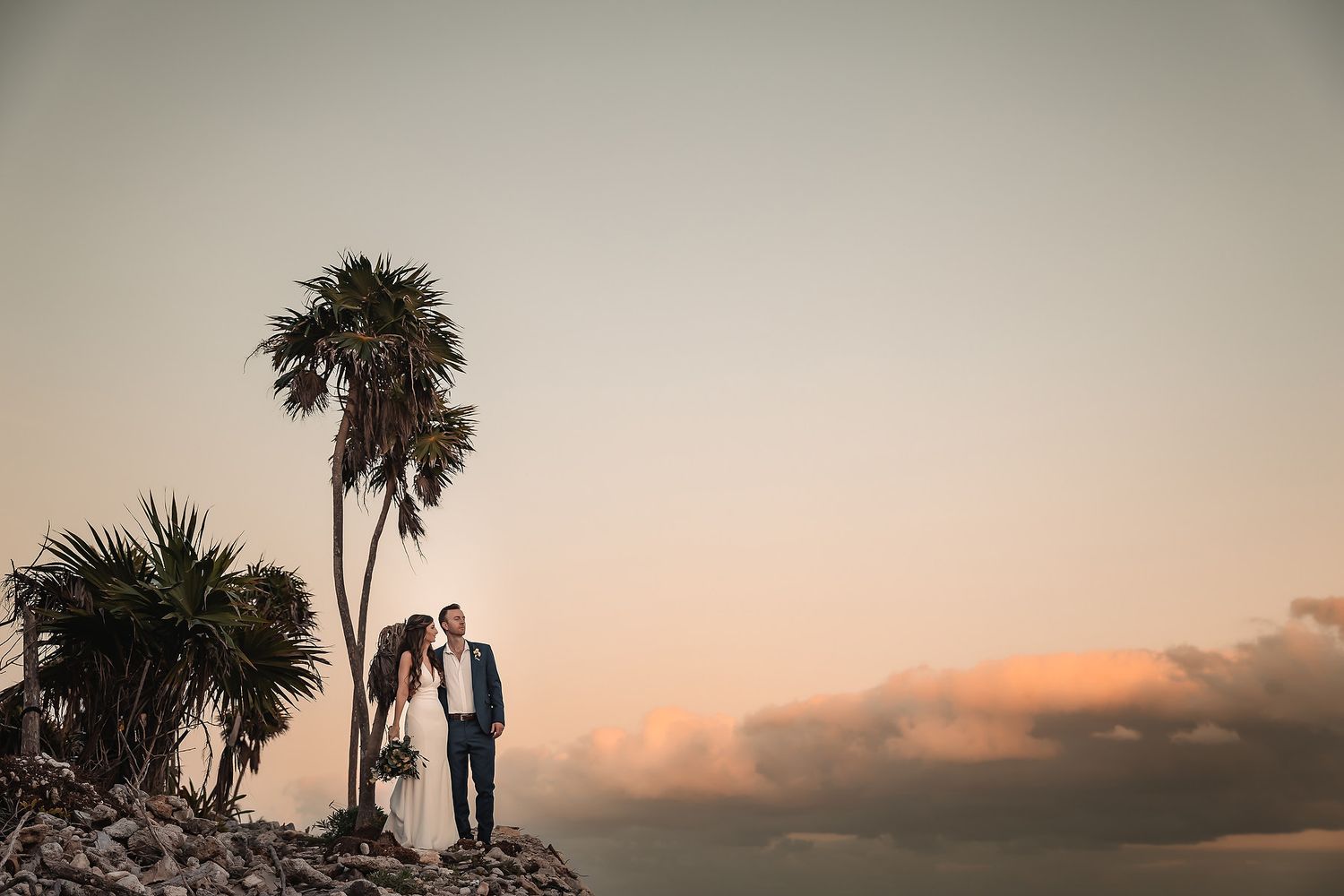 Silhouette of wedding couple against sunset sky with palm trees.