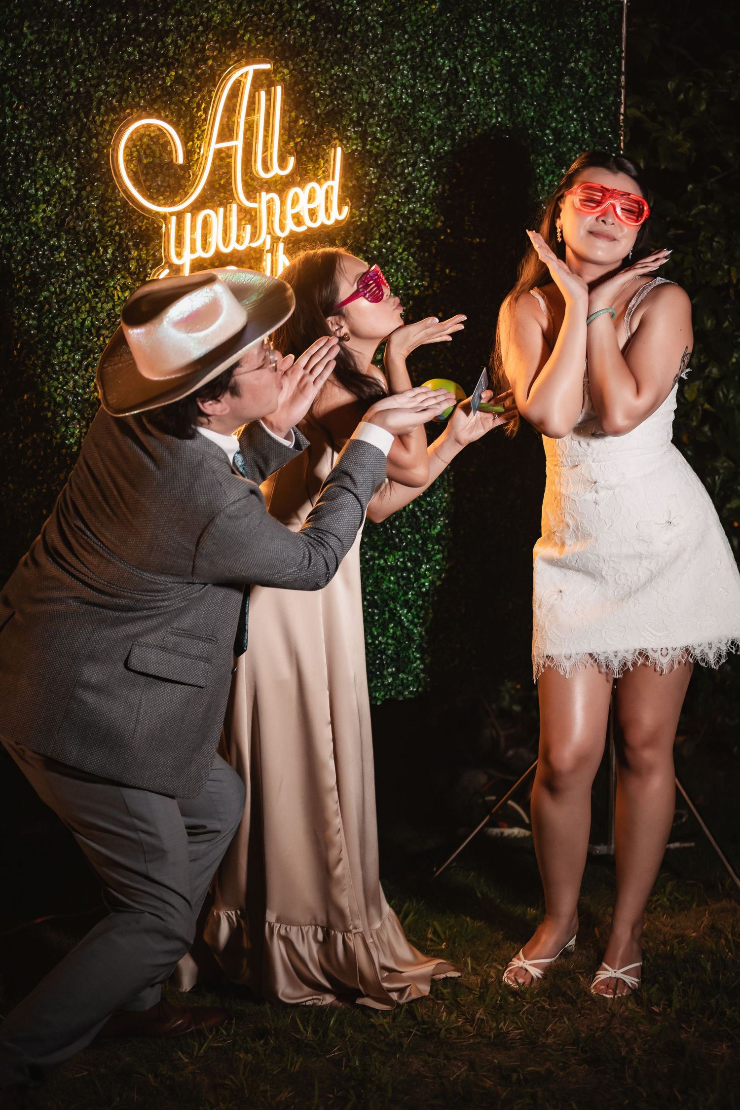 Fun wedding photo session with neon signs and creative poses against green backdrop.