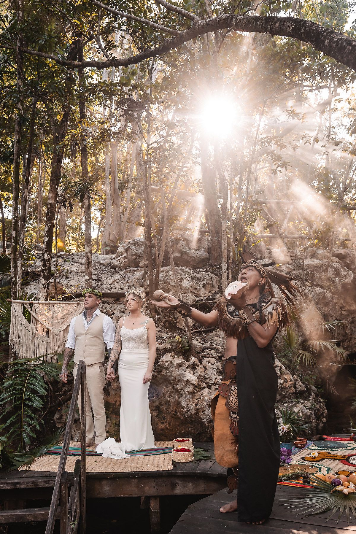 A wedding photoshoot in progress at a tropical outdoor location with sunlight streaming through the trees.