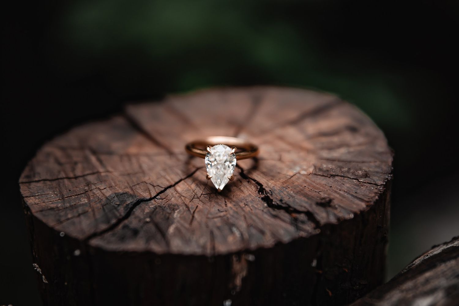 A diamond engagement ring sits on weathered wood in artistic macro photography.