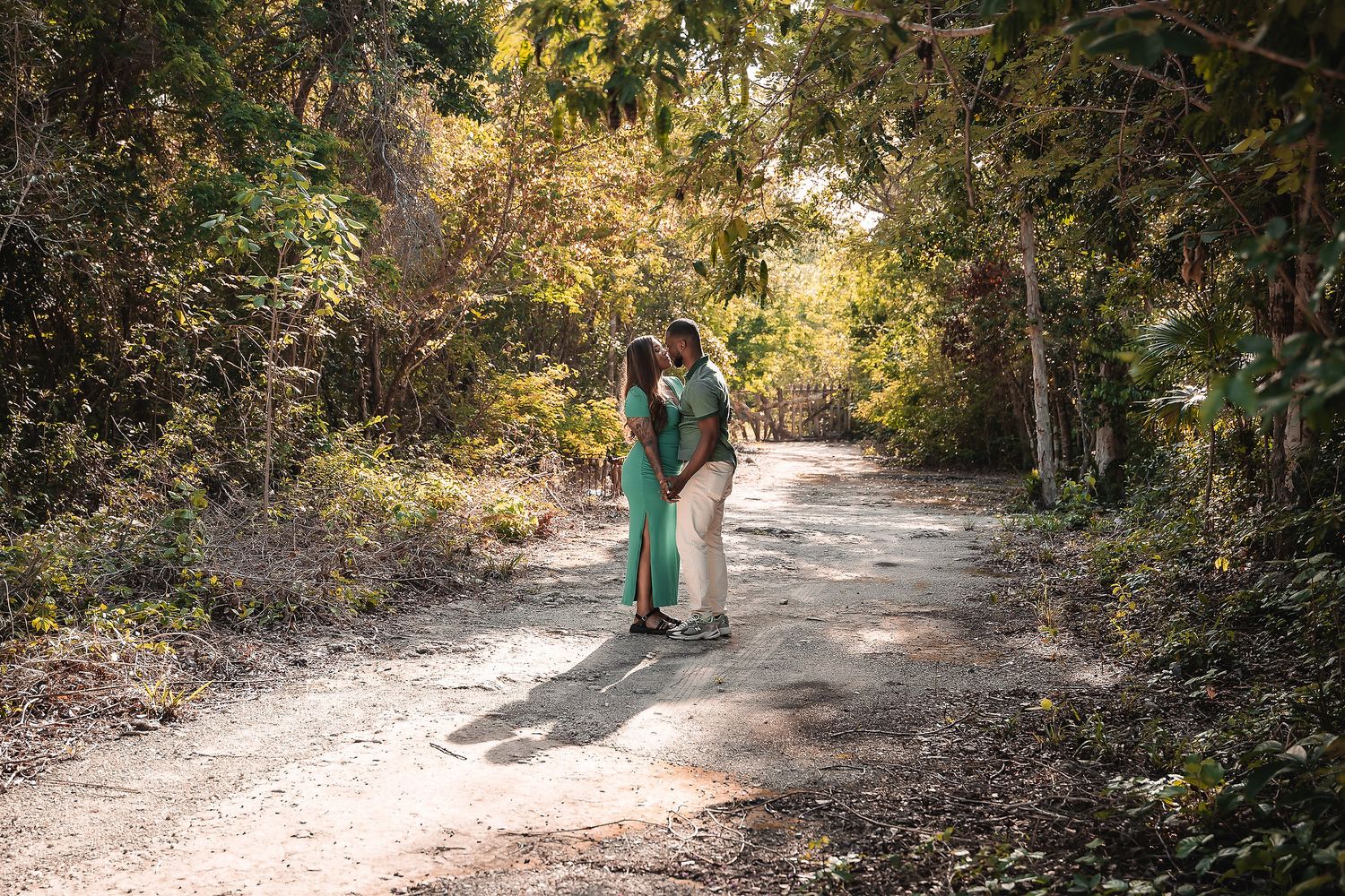 A couple walks hand in hand along a sunlit forest path during an engagement photoshoot.