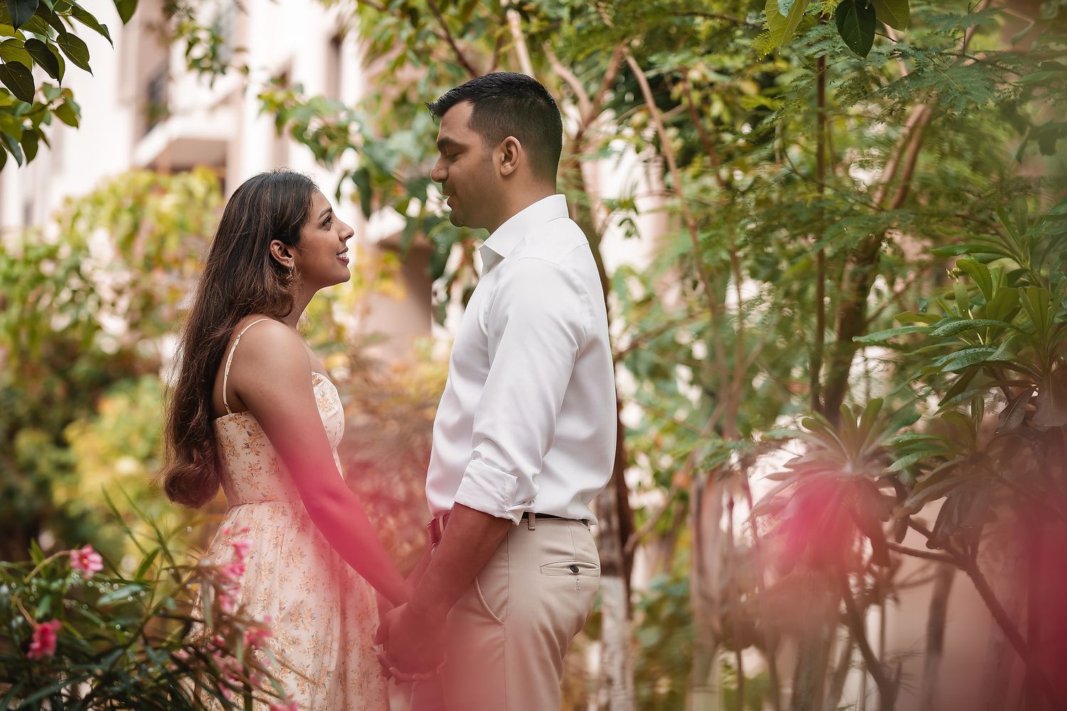 Couple embraces while walking through a lush garden pathway with dappled sunlight.