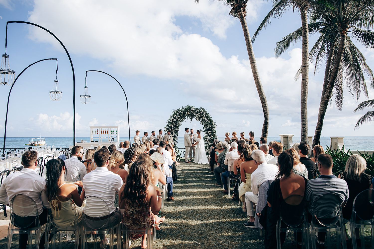A beachside wedding ceremony setup with white chairs and floral arch overlooking the ocean.
