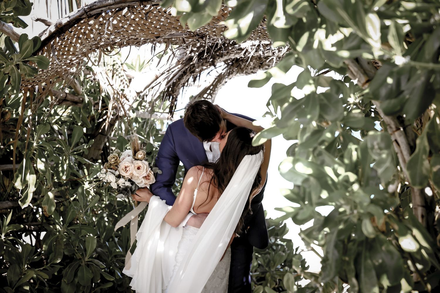 Wedding couple sharing intimate moment among green foliage.