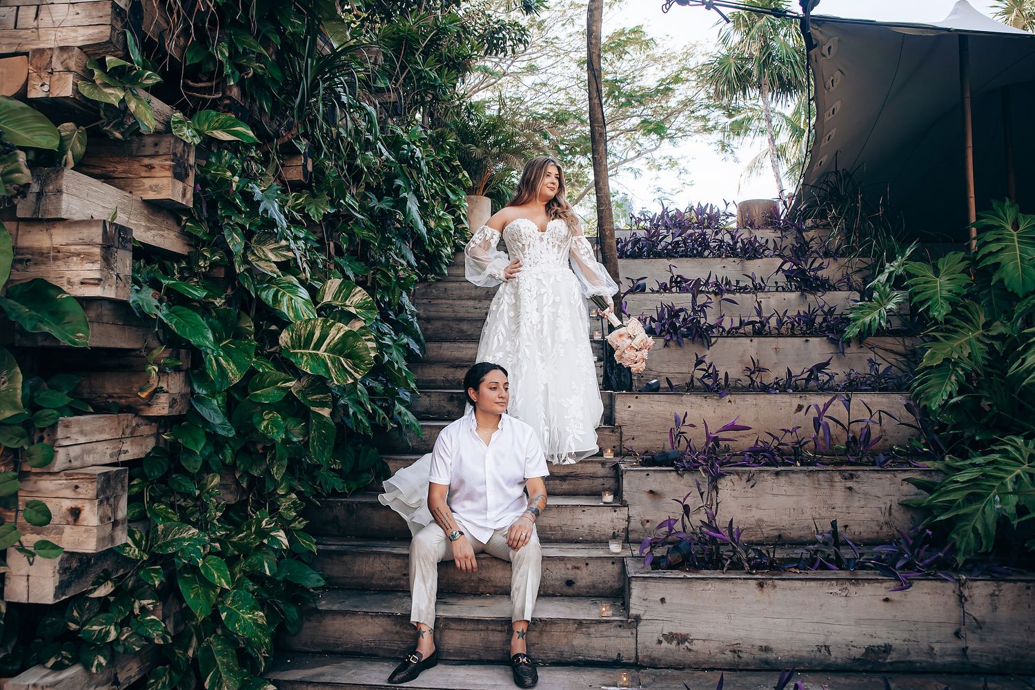 Wedding couple poses together on rustic stone steps surrounded by tropical greenery.