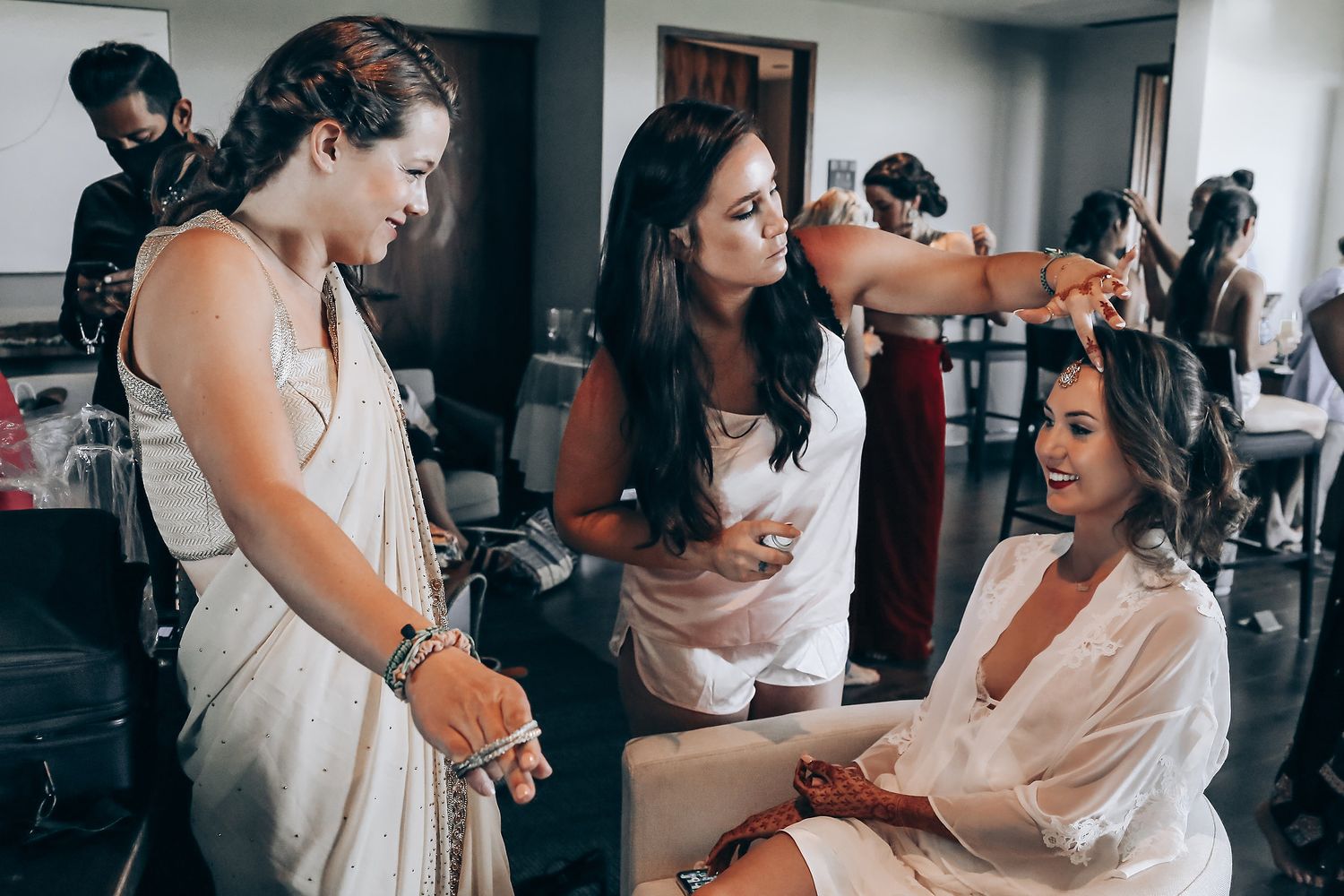 A group getting ready in a bridal suite, with white dresses and preparations underway in a bright indoor setting.