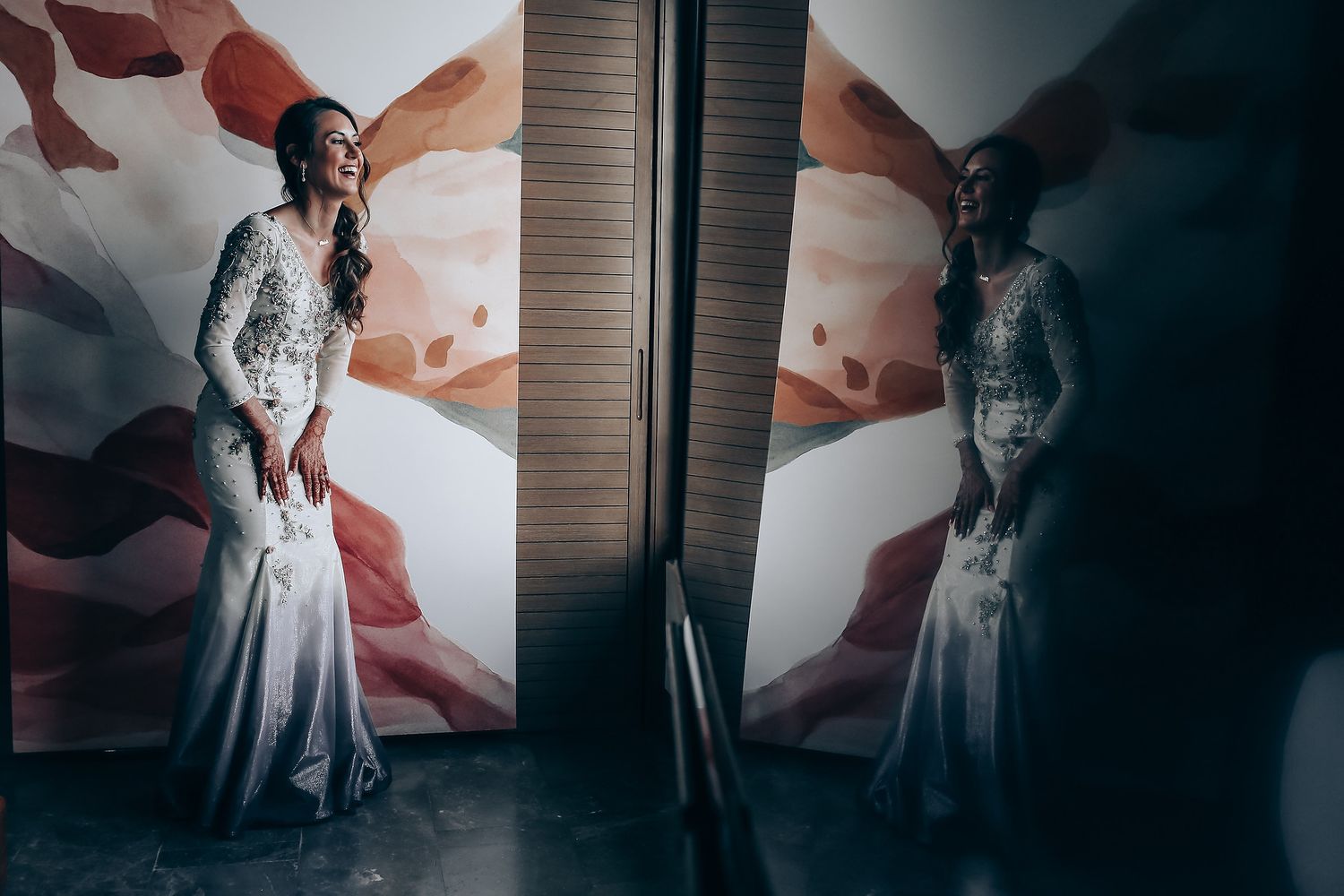 A couple in wedding attire poses against a dramatic red and white abstract wall in a modern interior space.