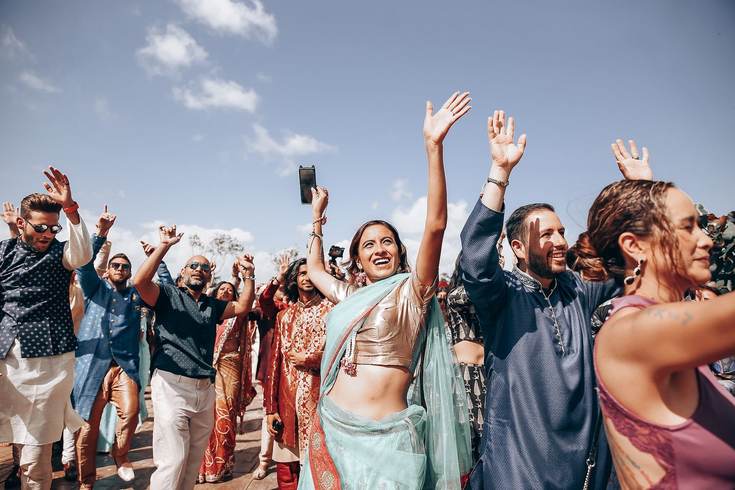 Joyful wedding guests raising their hands in celebration outdoors during a festive ceremony.