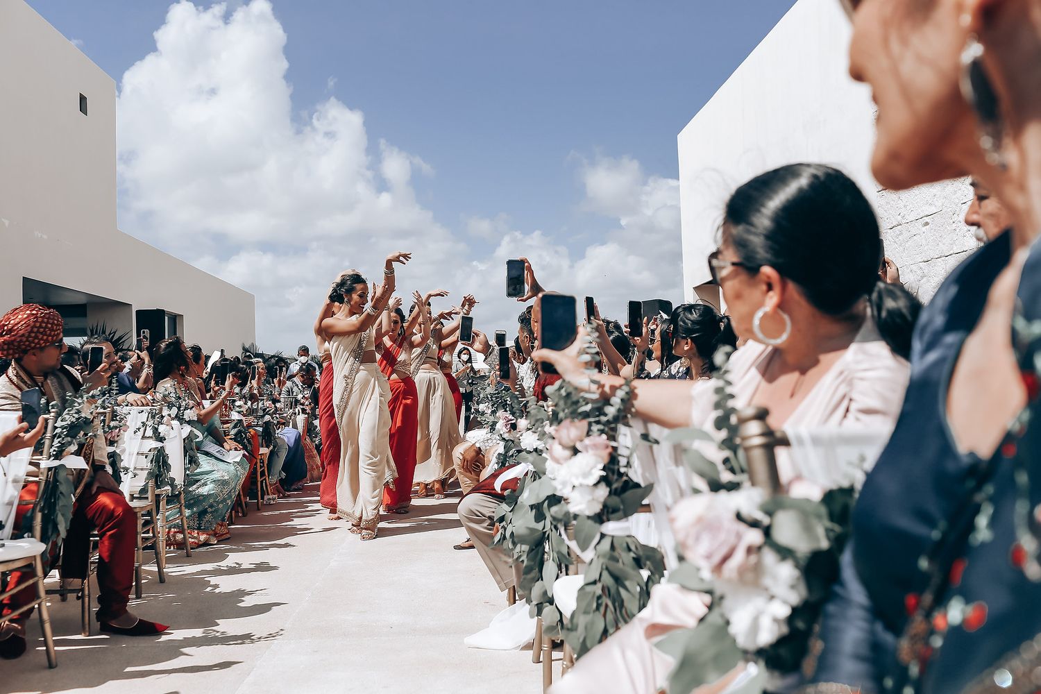Wedding guests gather outdoors under blue skies for a celebration.