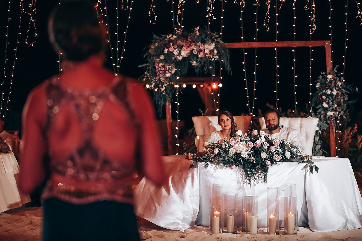 Elegant wedding reception table decorated with white linens and floral arrangements under twinkling string lights.