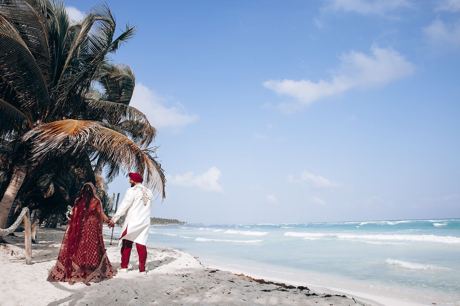 Scenic beach wedding photography with turquoise ocean waves and palm trees in the background.
