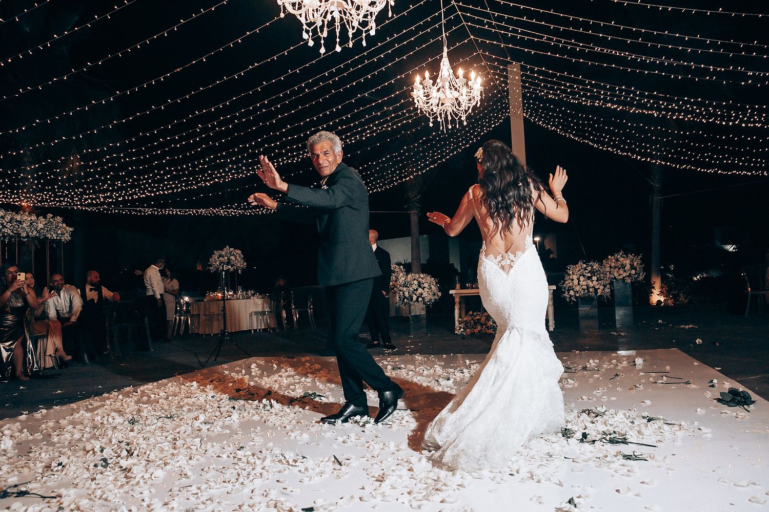 Wedding celebration on a dance floor decorated with hanging fairy lights and crystal chandeliers.