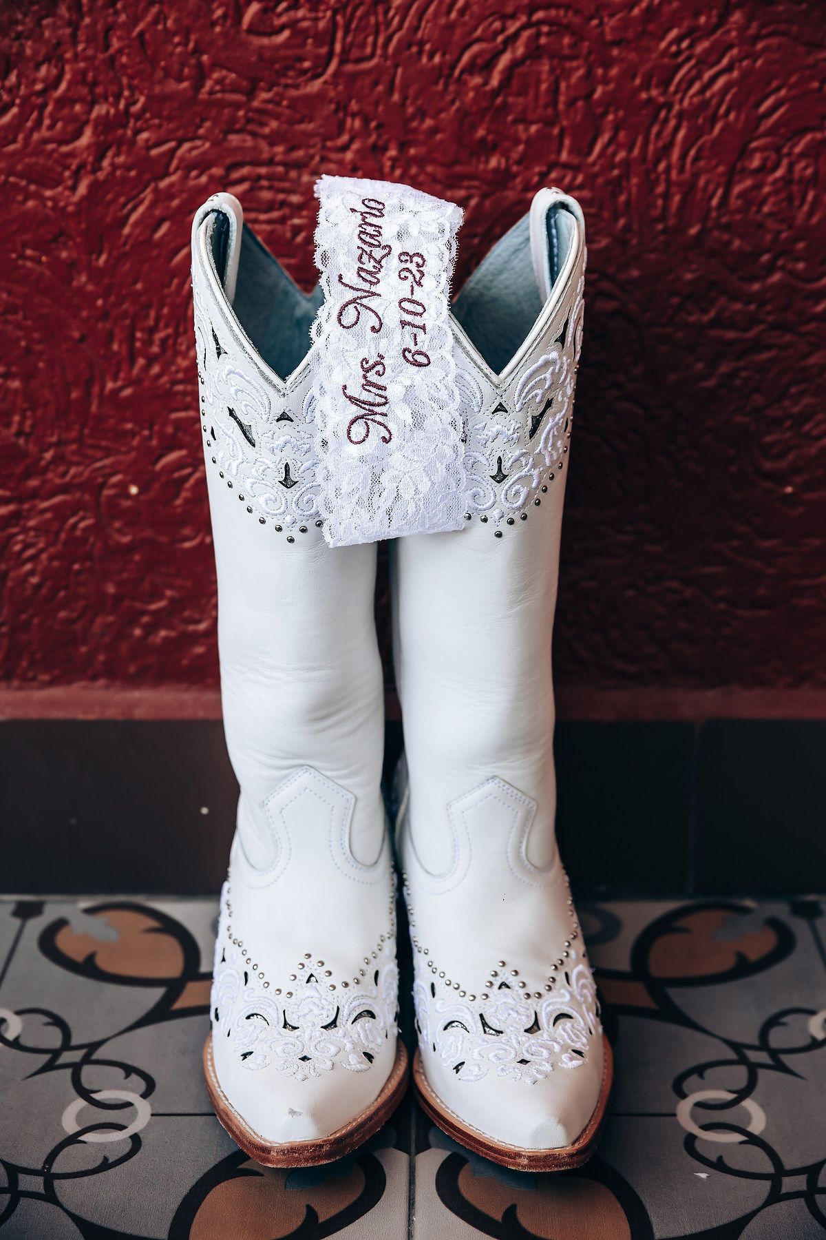 White leather cowboy boots with intricate cutout details against a red textured wall.