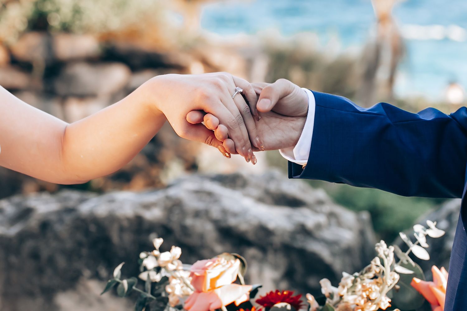 Close-up of hands joining together during outdoor wedding ceremony.