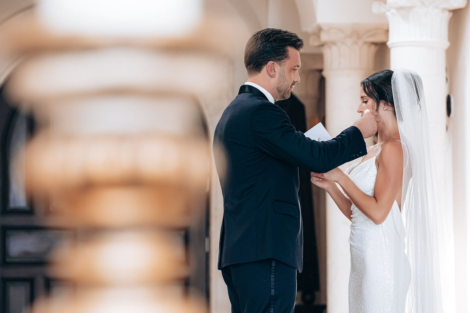 A romantic wedding couple shares intimate moments in an elegant white interior hallway with soft natural lighting.