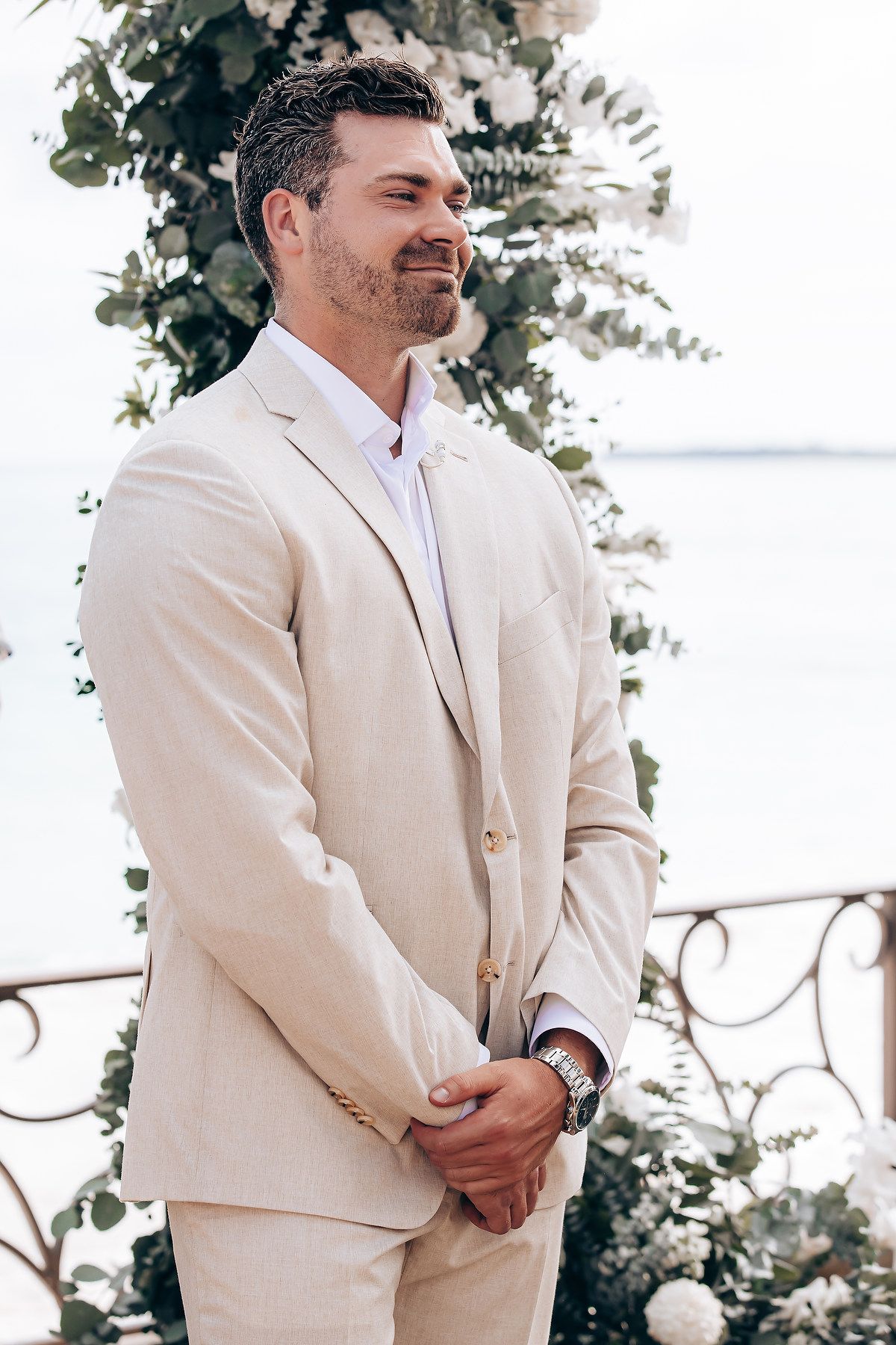 Three groomsmen in cream-colored suits stand together during an outdoor wedding ceremony.
