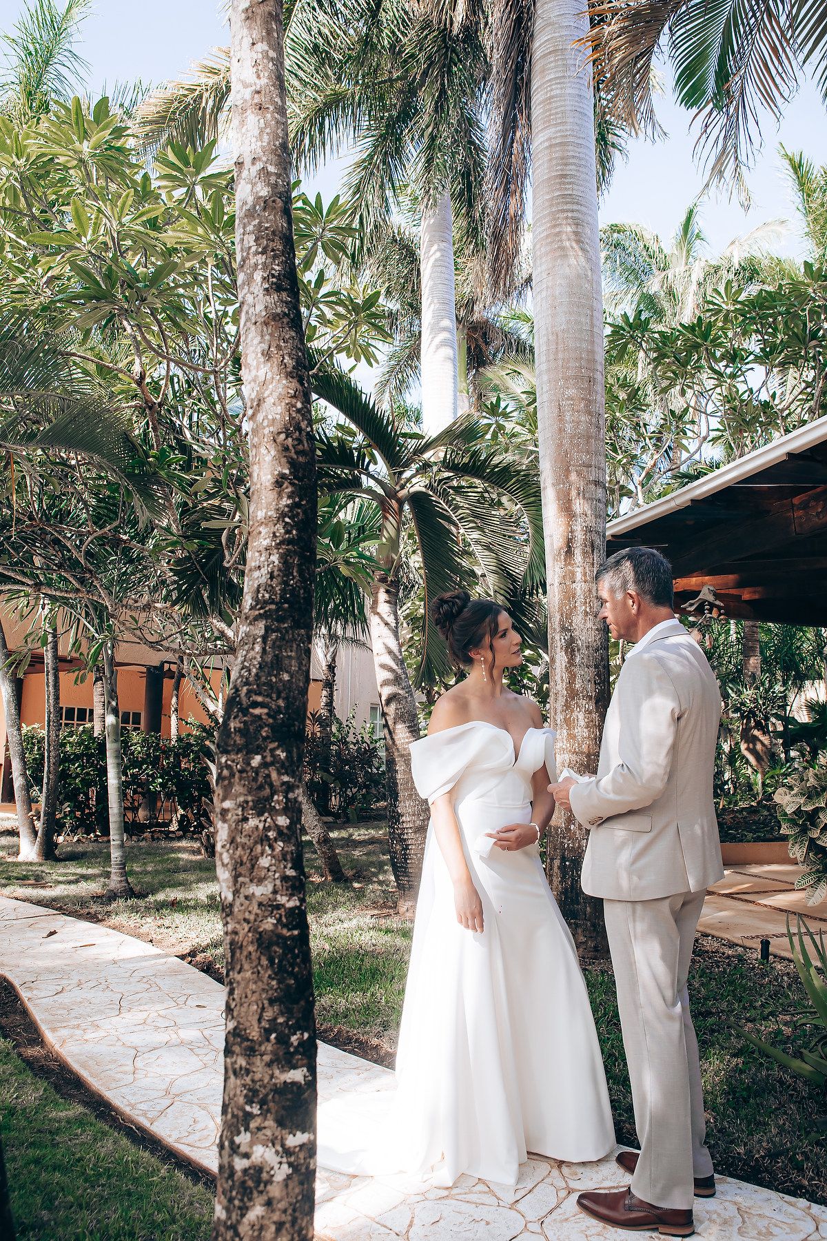A couple in white attire shares intimate moments among palm trees in a tropical garden setting.