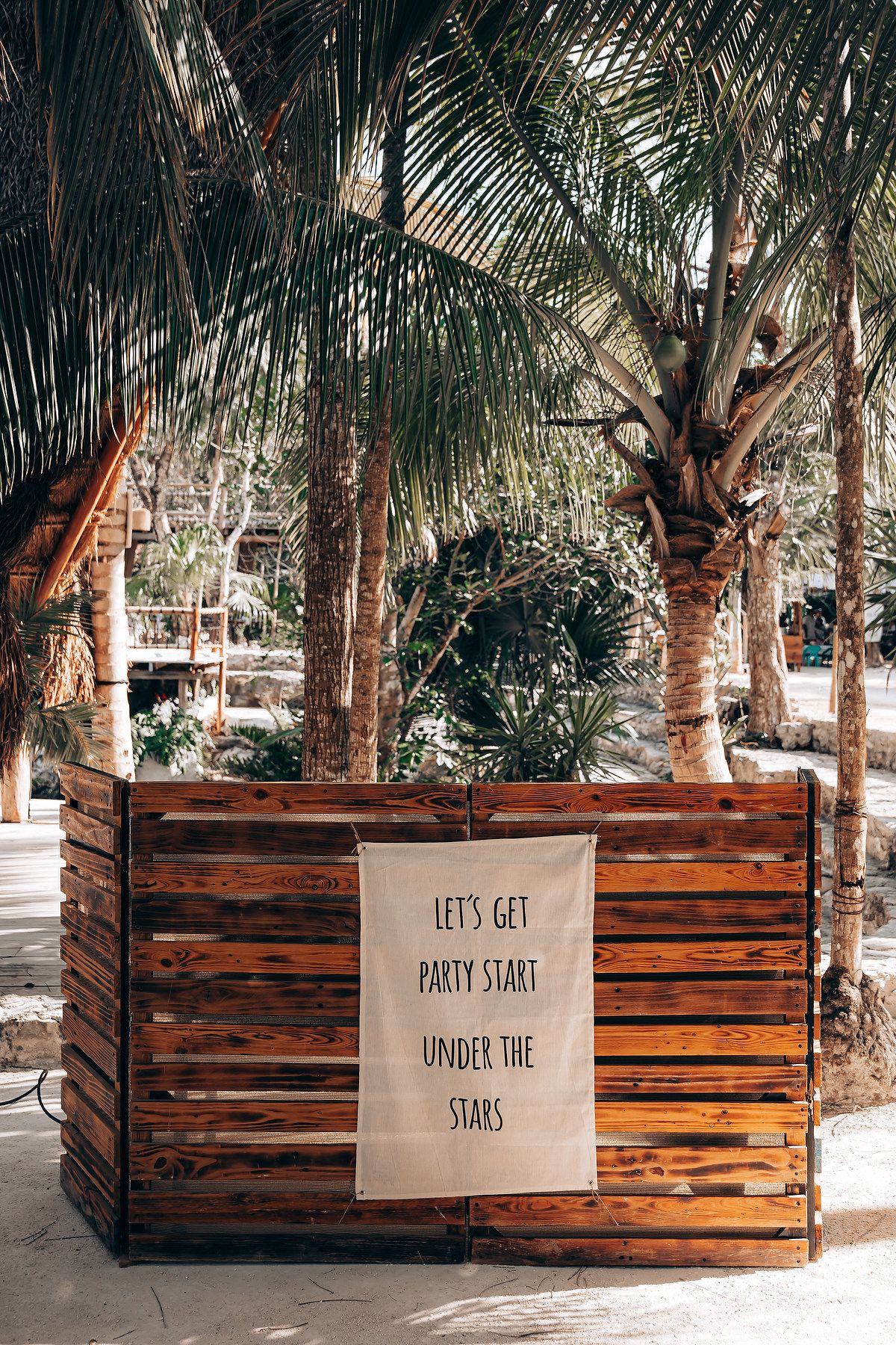 A series of wooden planter boxes with inspirational text signs displayed among palm trees in a tropical setting.