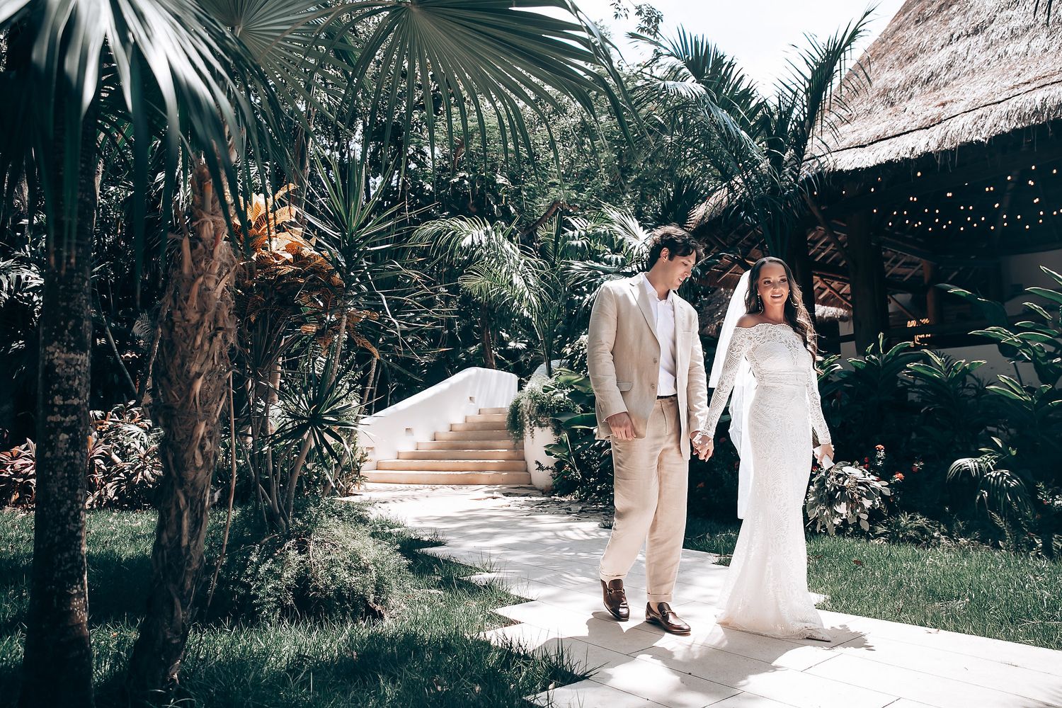 Wedding ceremony setup with white chairs and tropical garden backdrop.