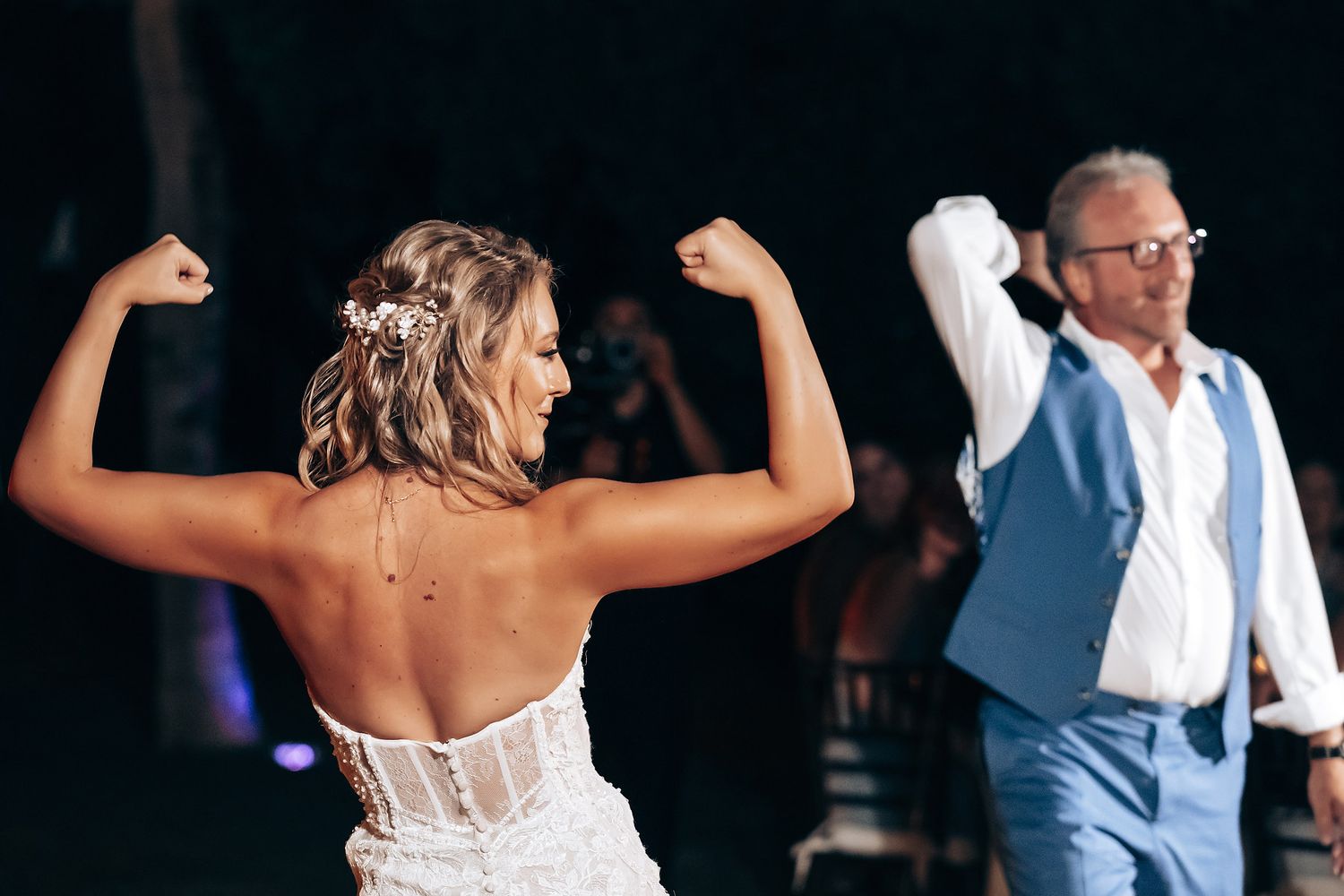 Wedding couple and guests dance joyfully together on a dance floor at an evening reception celebration.