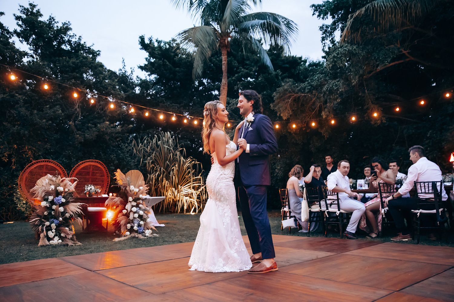 Wedding reception under string lights at dusk with guests dancing on an outdoor patio.