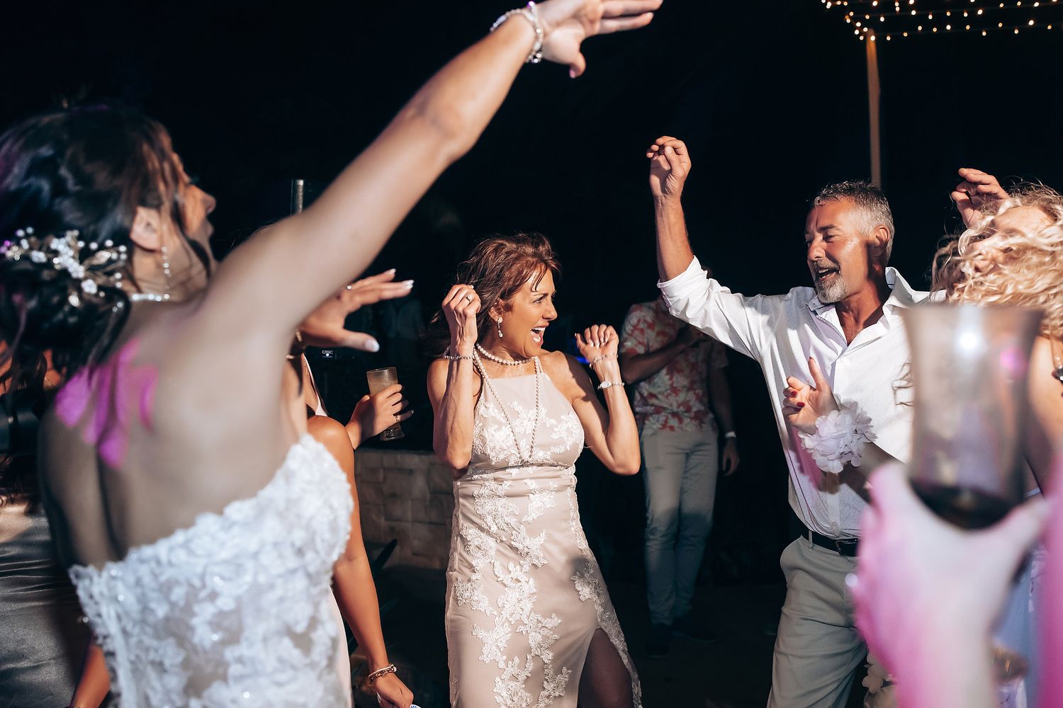 Wedding guests dancing and celebrating together on a dimly lit dance floor with string lights overhead.