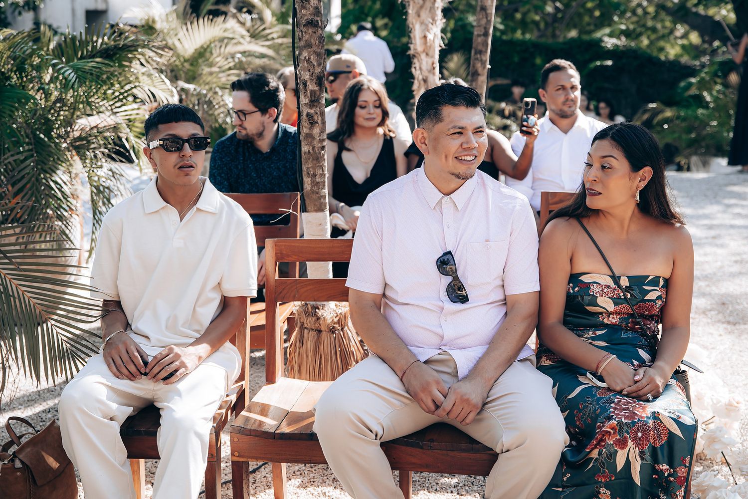 A group of people sitting and laughing together on wooden benches in an outdoor tropical setting.