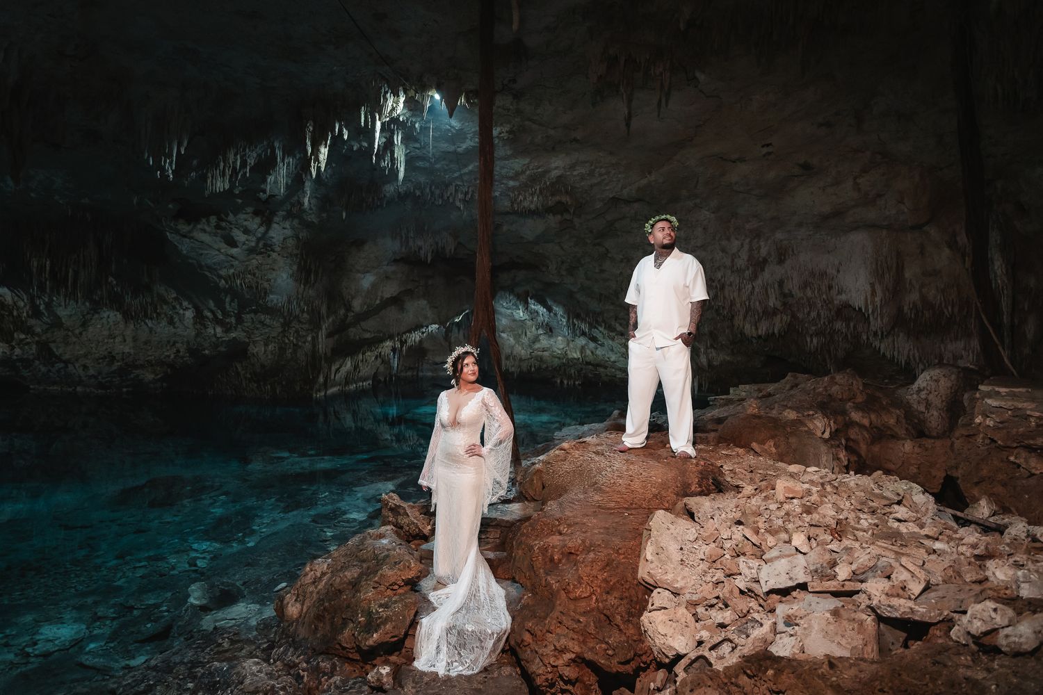Dramatic wedding portrait in a limestone cave with glowing turquoise waters.