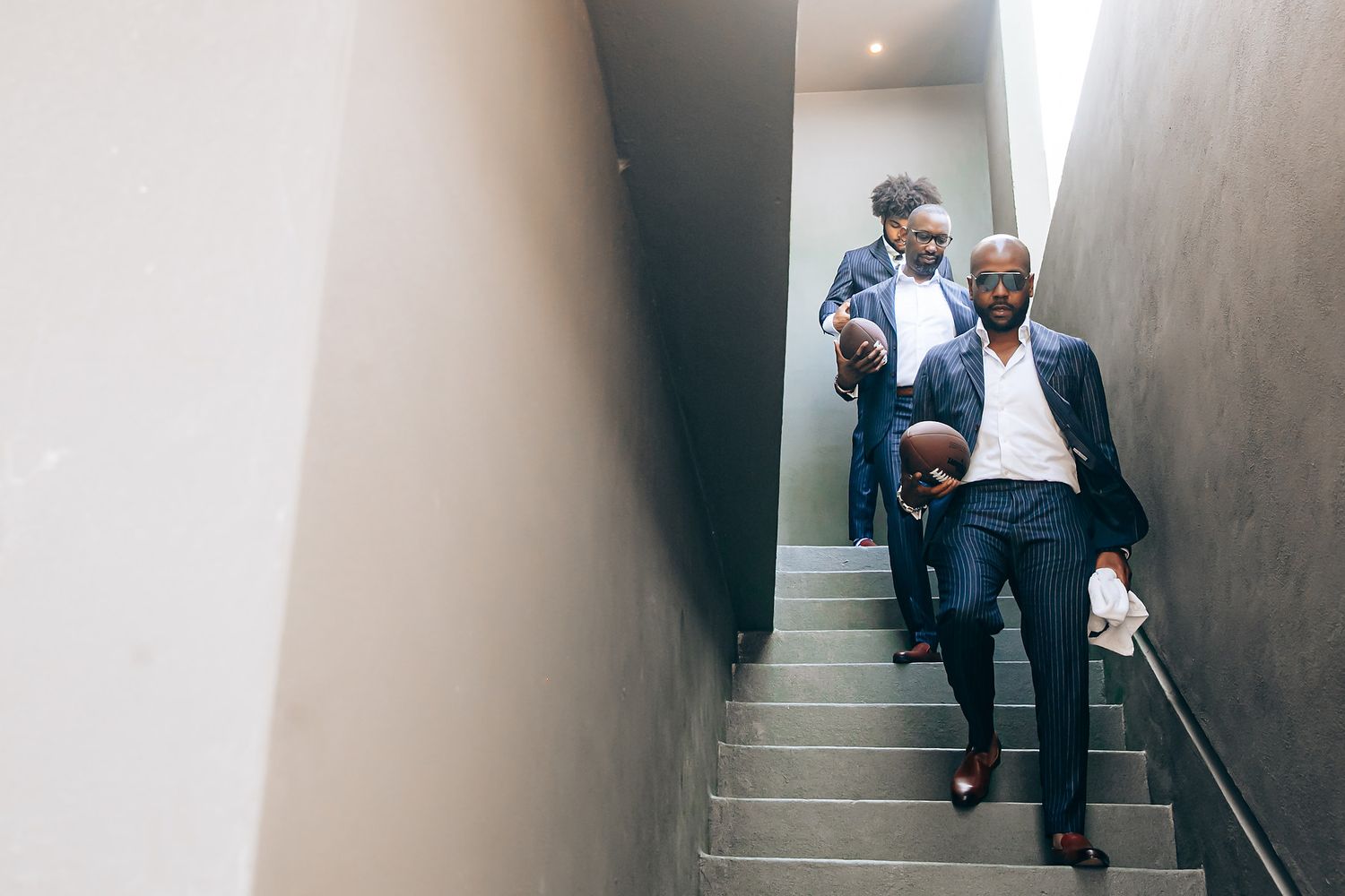 Two people in business attire walk down a grey concrete hallway with angular walls and dramatic lighting.