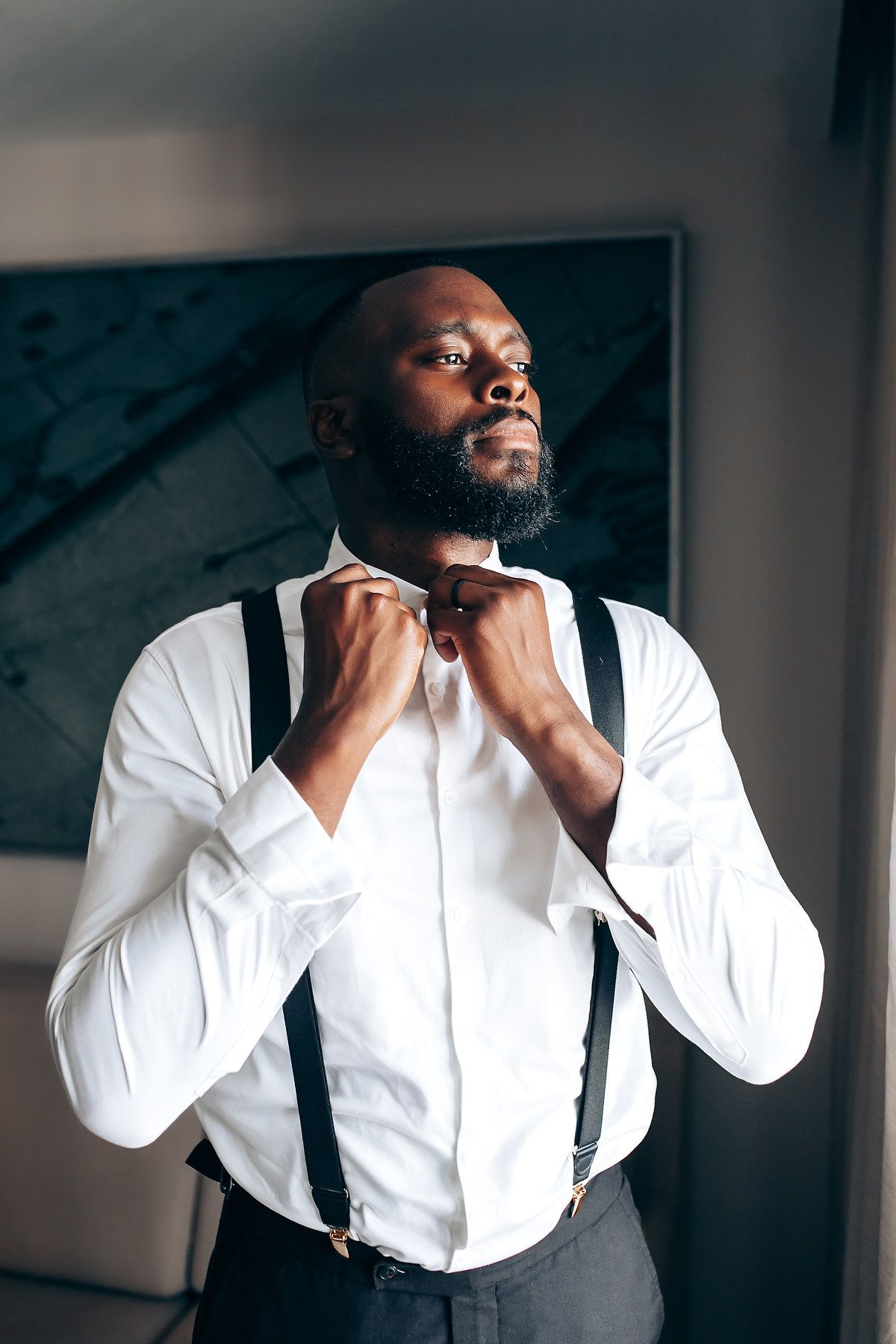 A groom adjusts his bowtie while wearing a crisp white shirt and black suspenders.