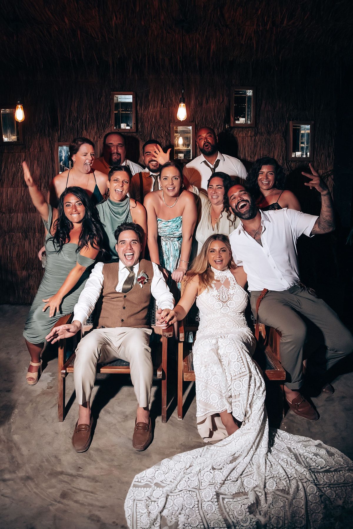Wedding celebration group photo on beach with guests in white and beige attire.