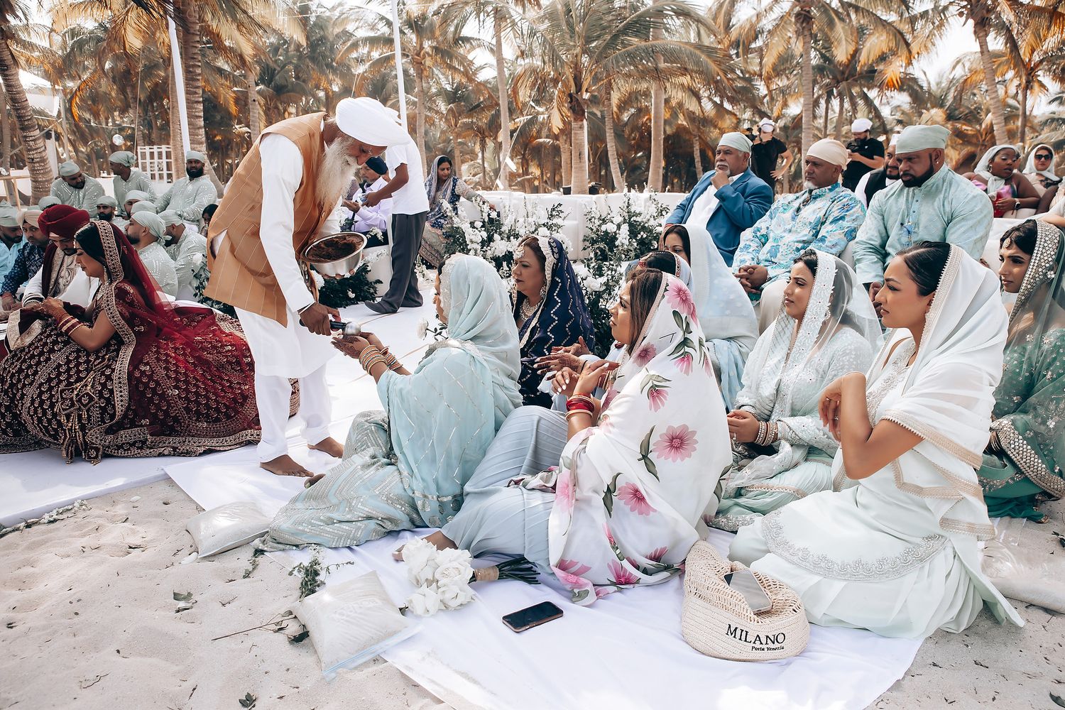 Beach wedding ceremony setup with palm trees and guests seated on white chairs.