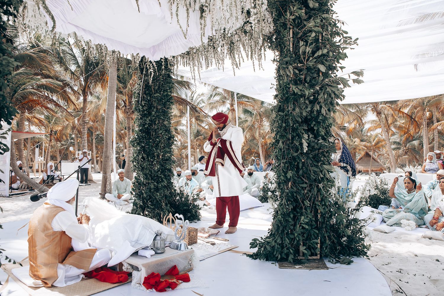 Outdoor wedding ceremony setup with white decor and greenery under palm trees.