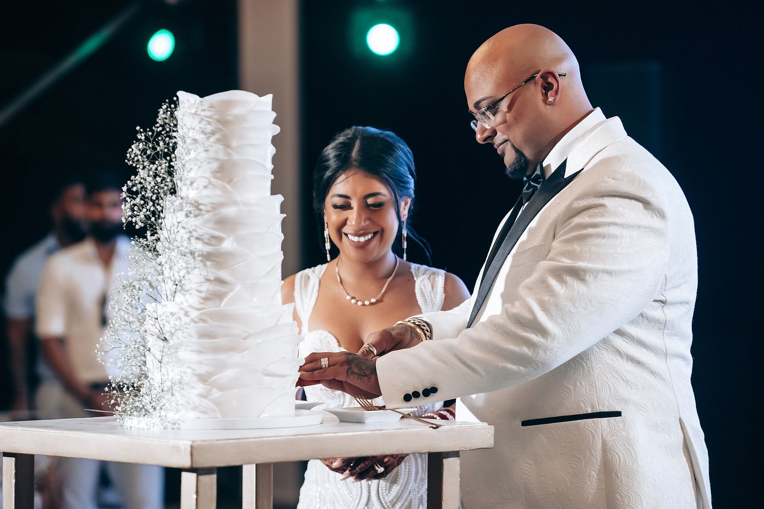 Newlyweds share a joyful moment while cutting their tall white wedding cake at their reception.
