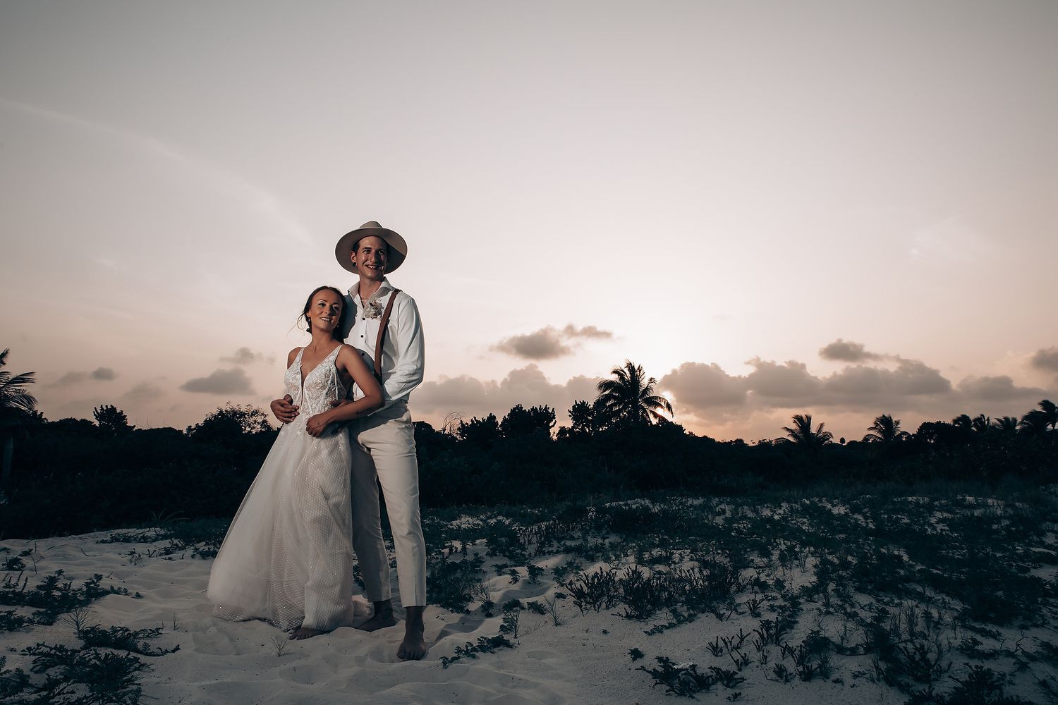 A romantic sunset portrait of a couple in wedding attire on a sandy beach.
