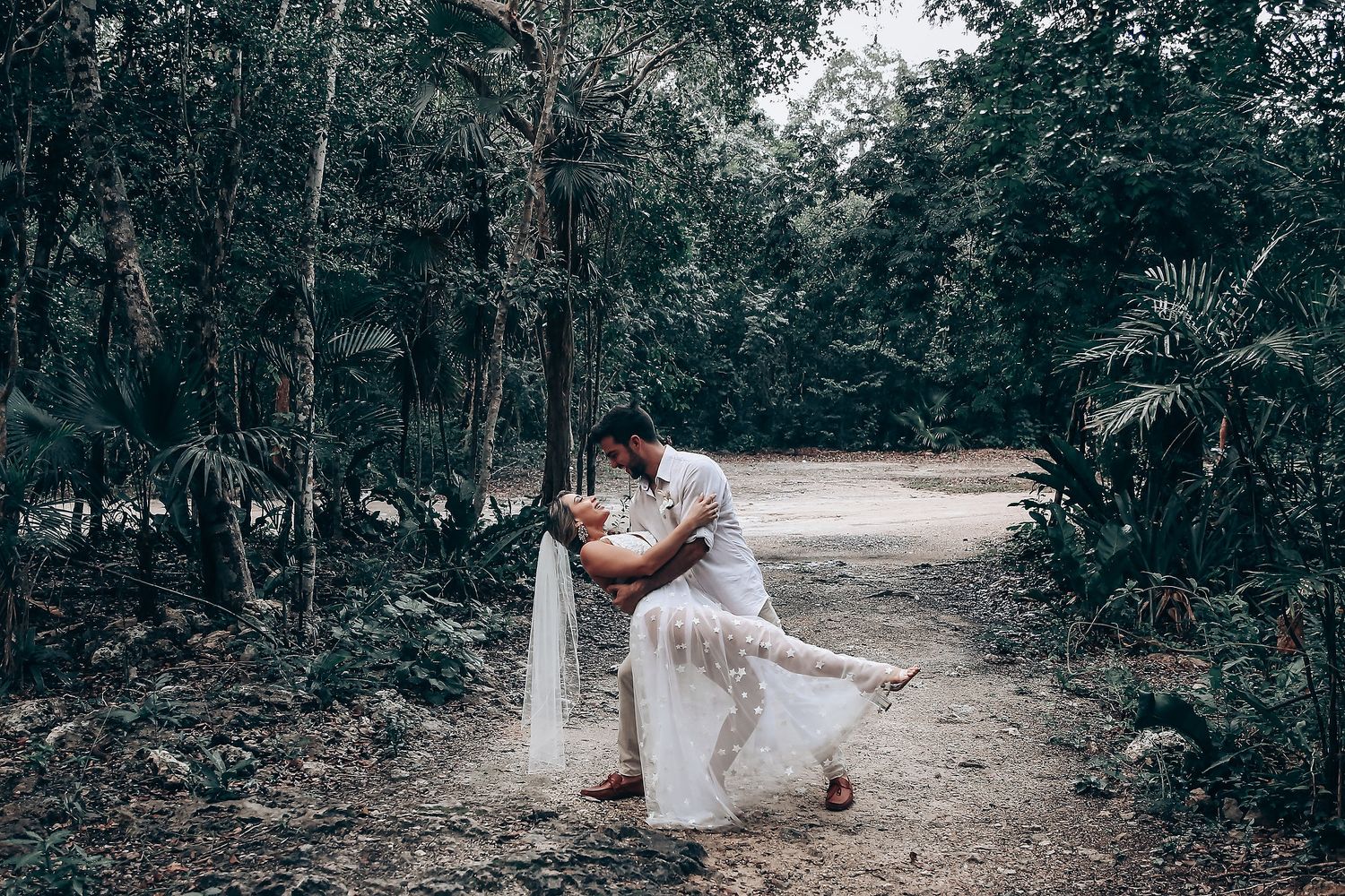 A path winds through a lush forest setting with people in white clothing visible in the distance.