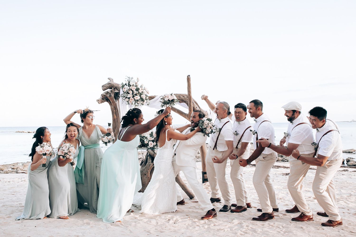 Wedding party posing playfully on a beach in coordinated white and mint green attire.