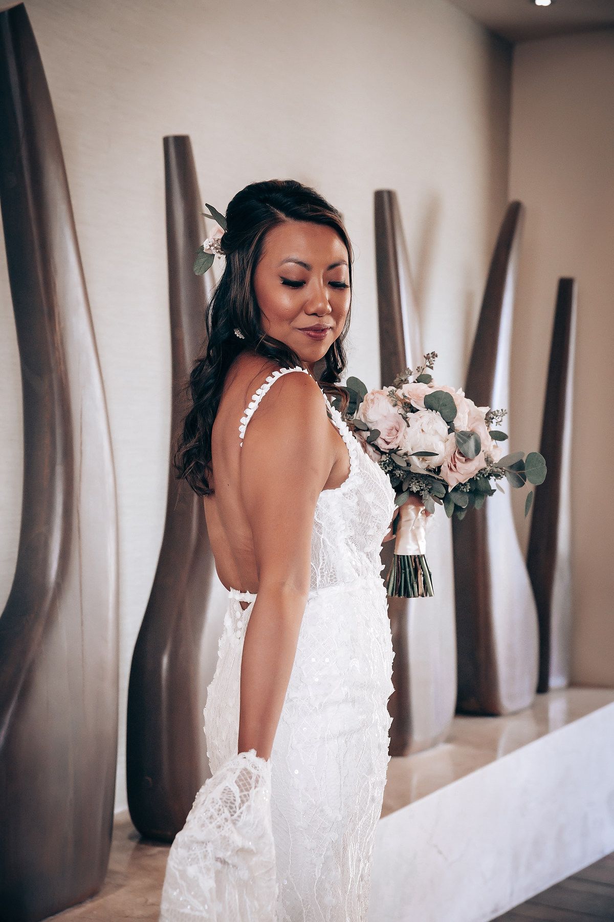 Stunning lace wedding dress photographed against neutral walls with a romantic bridal bouquet.