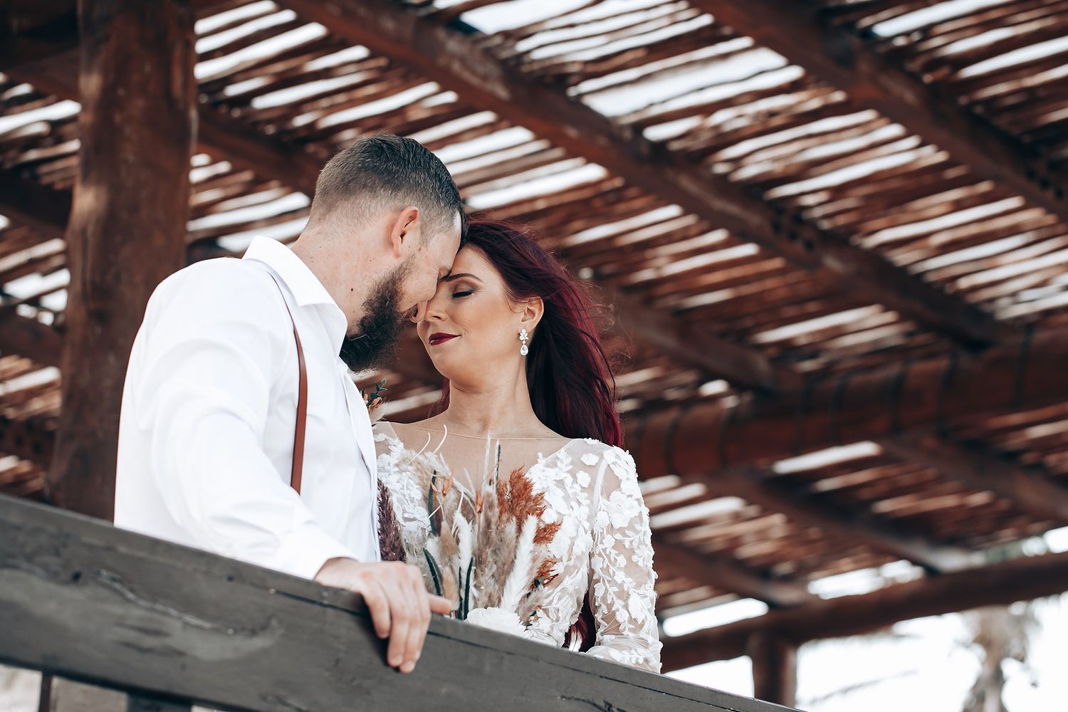 Romantic moment under wooden pergola during wedding photoshoot.