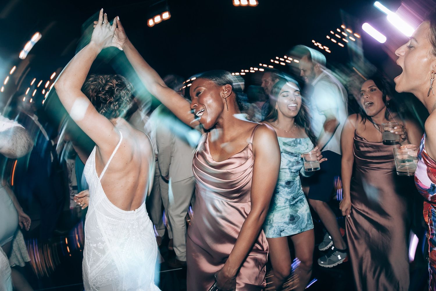 Wedding reception dance party with guests celebrating under atmospheric lighting.