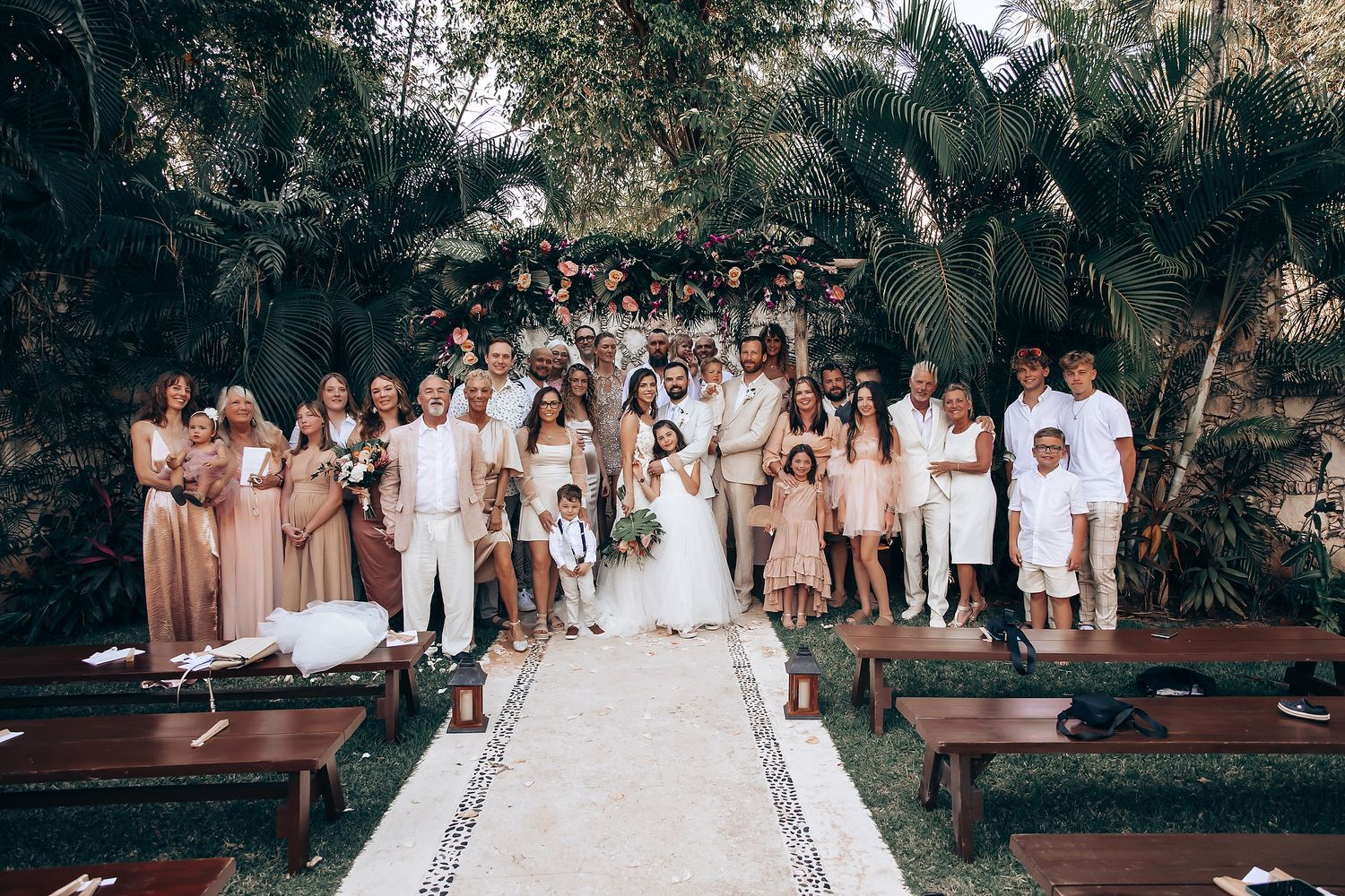 Wedding guests gathered outdoors in a tropical garden setting with palm trees and natural decor.
