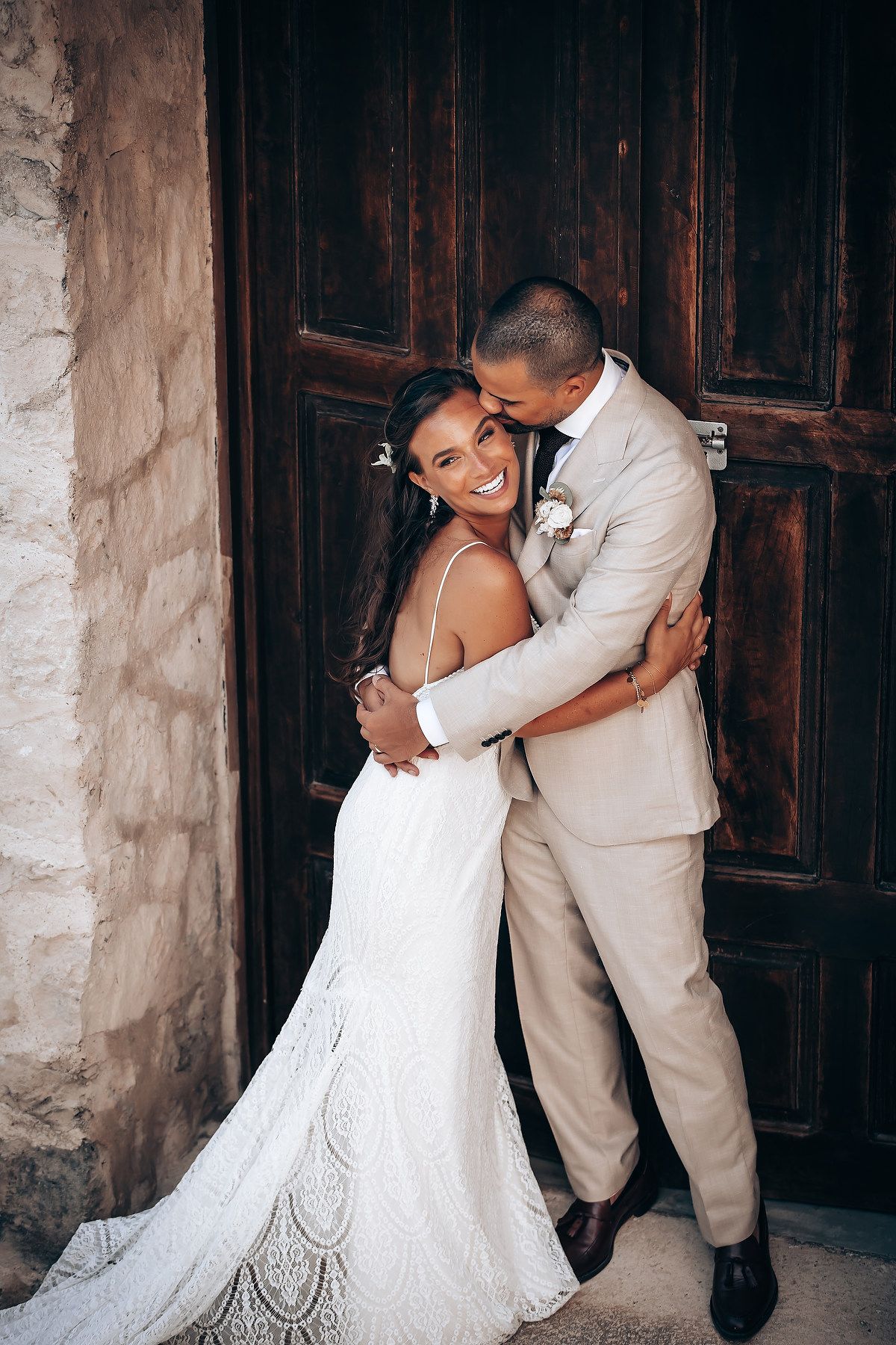 Wedding couple sharing playful moments against a rustic stone wall backdrop.