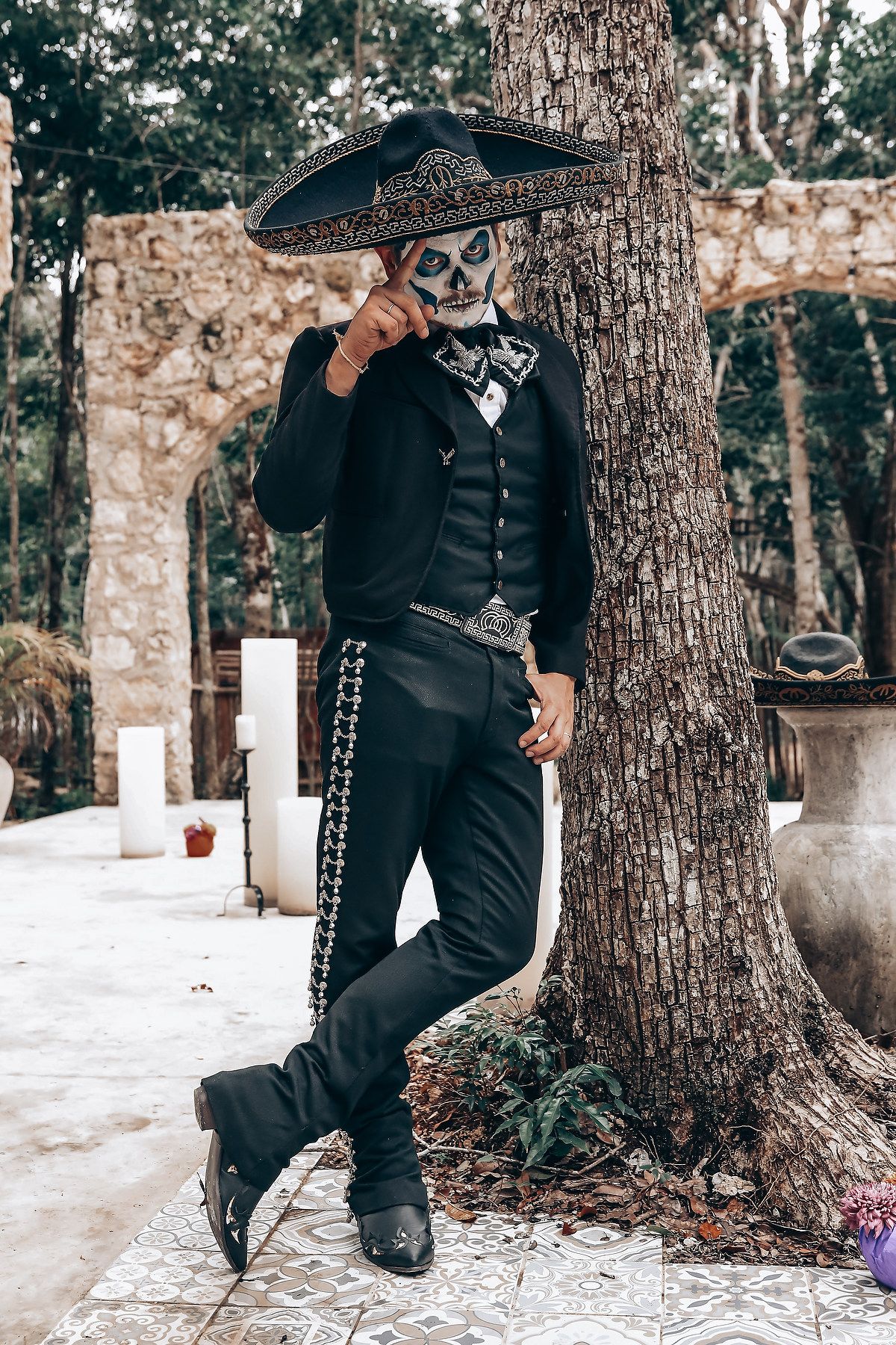 A figure in black mariachi attire and sombrero poses dramatically near tree trunks in snow.